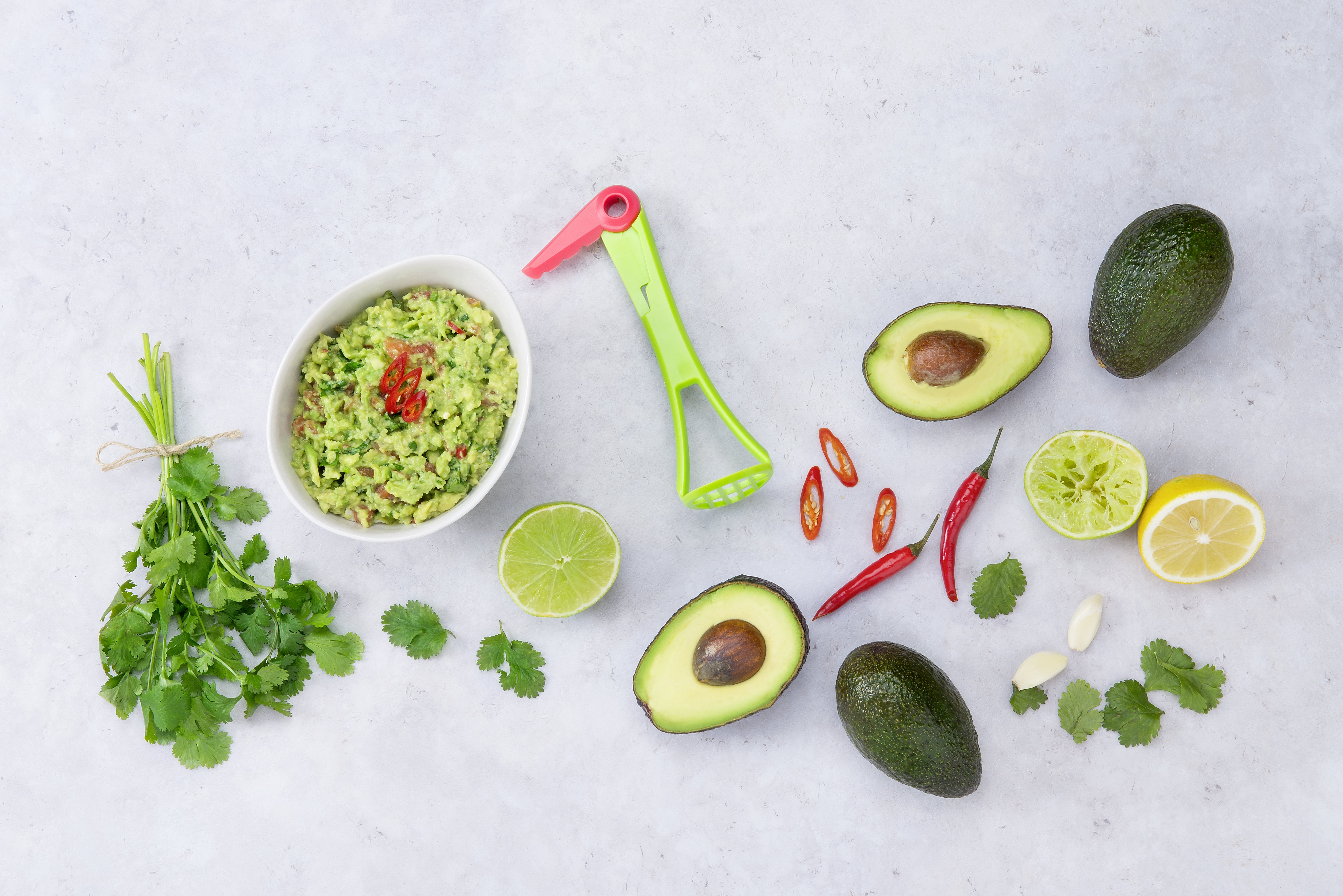 Guacamole-Zutaten: Schüssel mit Dip, Avocados, Limette, Zitrone, Koriander, Chilischoten, und Zerkleinerer.