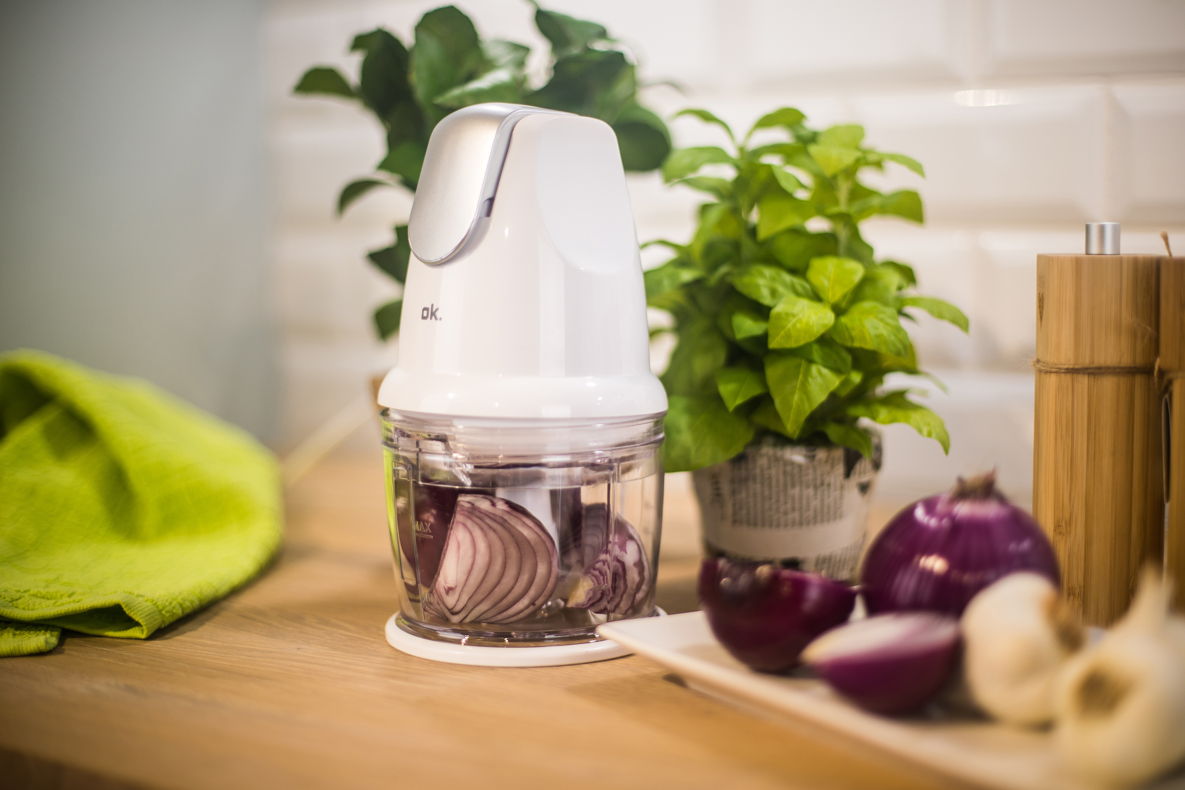 Ein weißer Zerkleinerer mit roten Zwiebeln, einem grünen Tuch und Topfpflanzen auf einer Holztheke.
