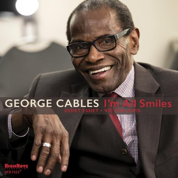 Ein Mann im Anzug lächelt. Text: George Cables I'm All Smiles. Rote Krawatte und Brille sind sichtbar.