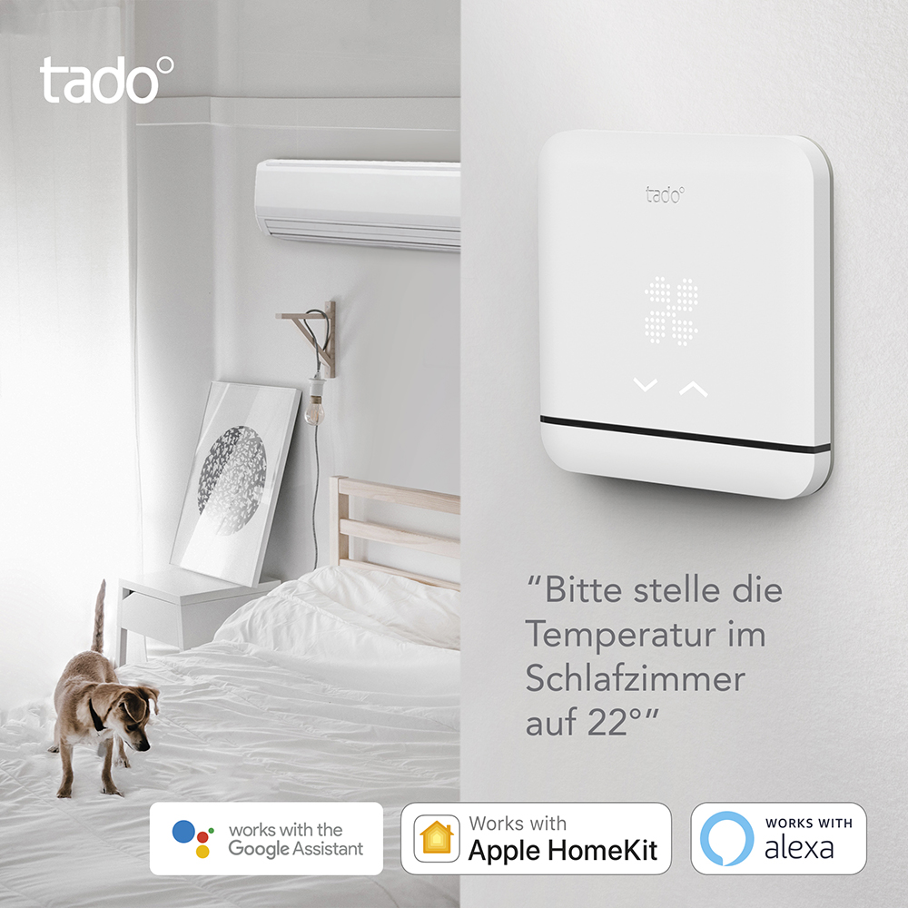 Weißes Smart-Thermostat an einer Wand. Ein Hund im Vordergrund, in der Nähe eines Bettes.
