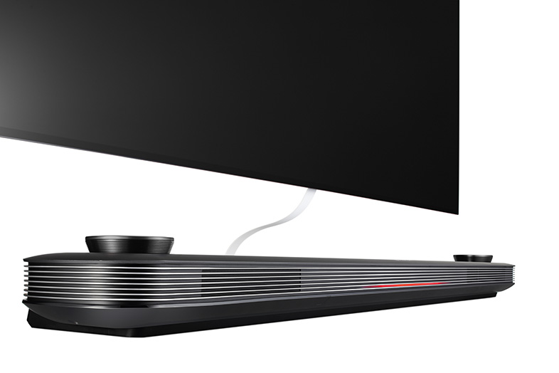Barra de sonido negra debajo de un televisor, con cable blanco y controles.