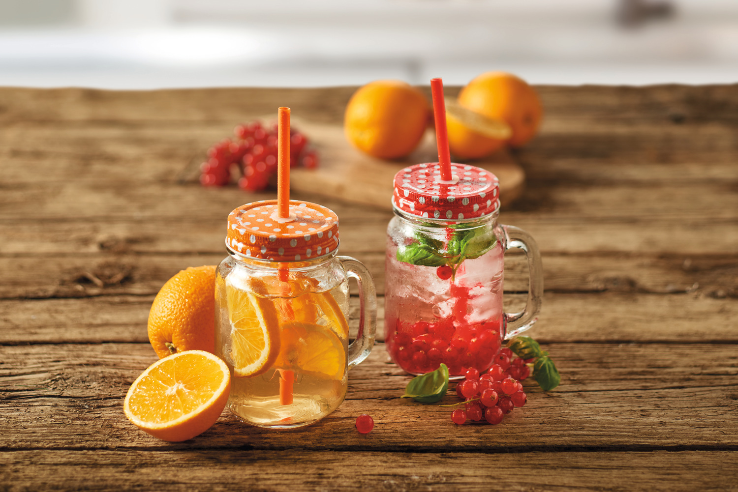 Zwei Einmachgläser mit Getränken, Orangen und roten Beeren auf einem Holztisch.