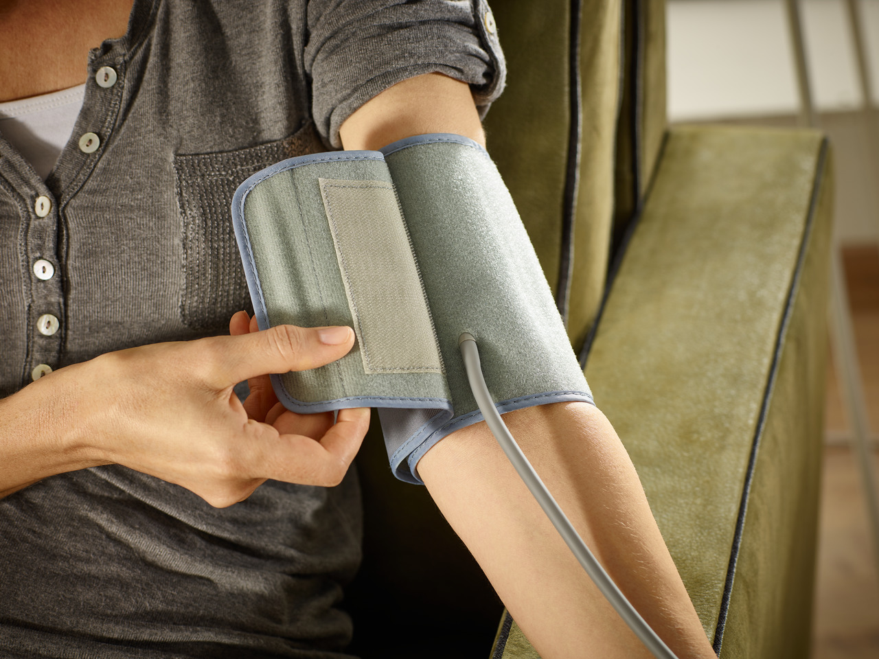 Person misst ihren Blutdruck. Arm mit Manschette. Die Person hält die Manschette.