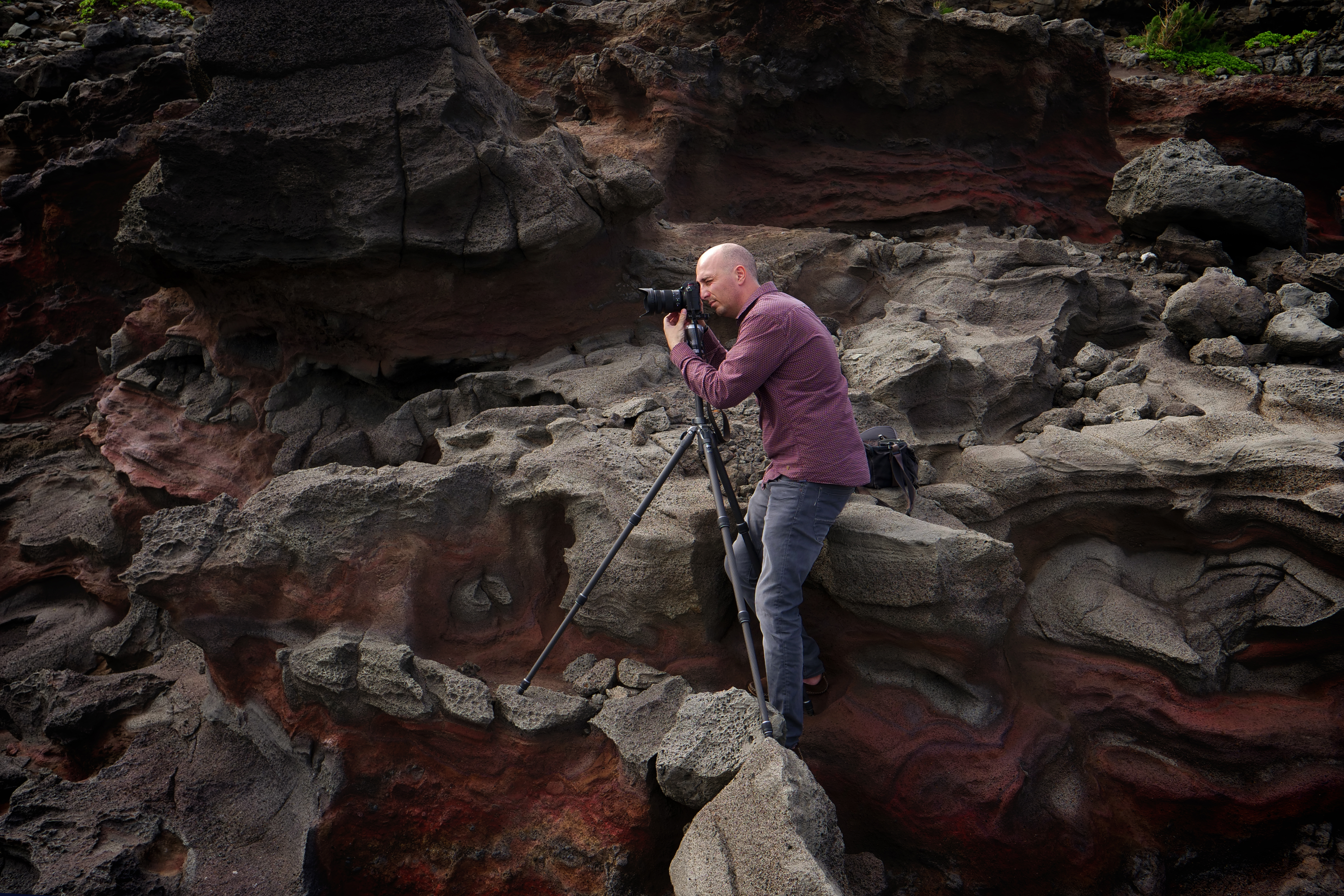 Ein Mann mit Kamera auf einem Stativ fotografiert rote und braune Felsen.