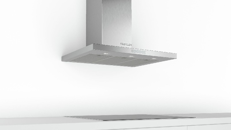 Una campana extractora de acero inoxidable montada en una pared blanca sobre una encimera negra.