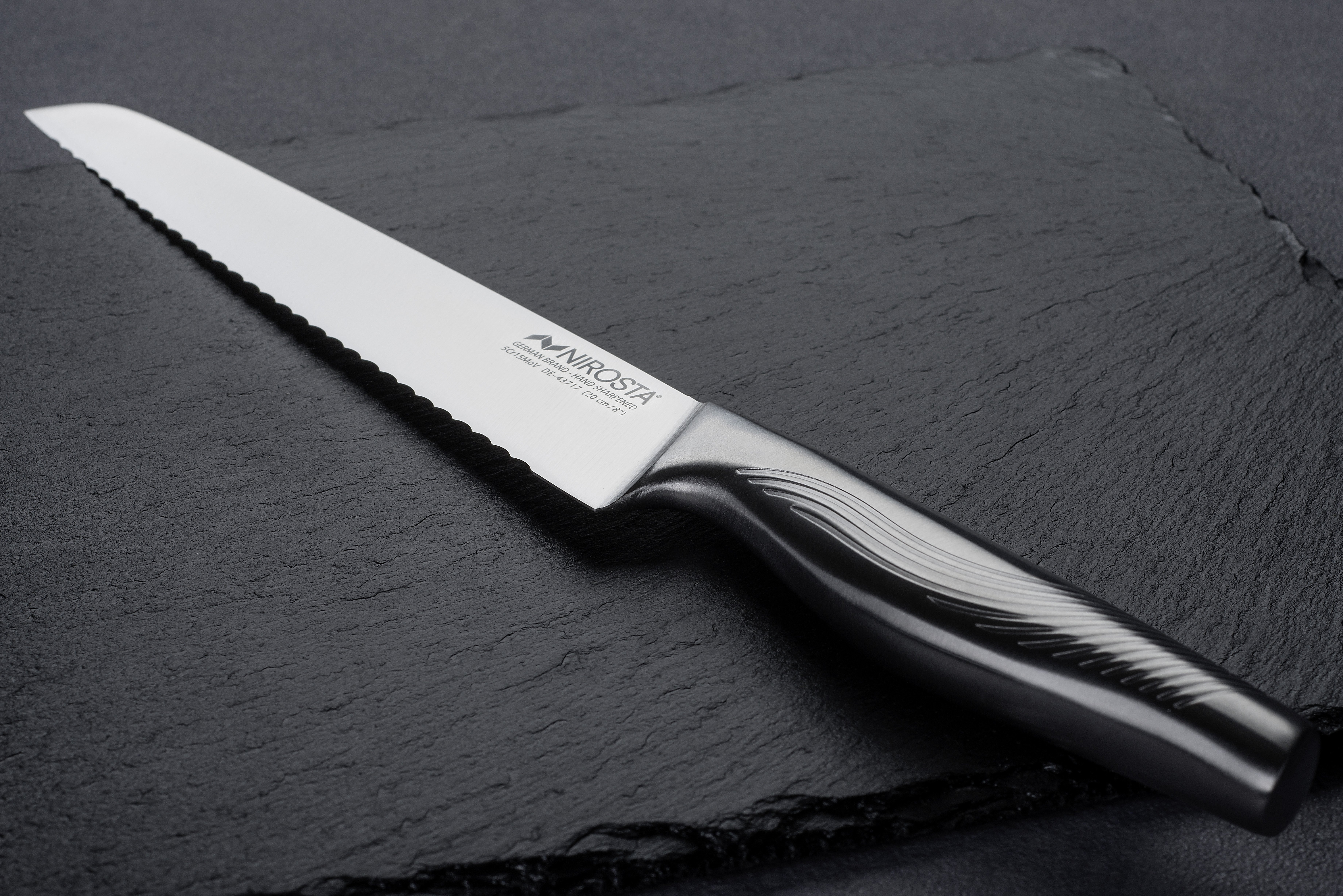 Silbernes Messer mit Wellenschliff auf schwarzer Oberfläche.