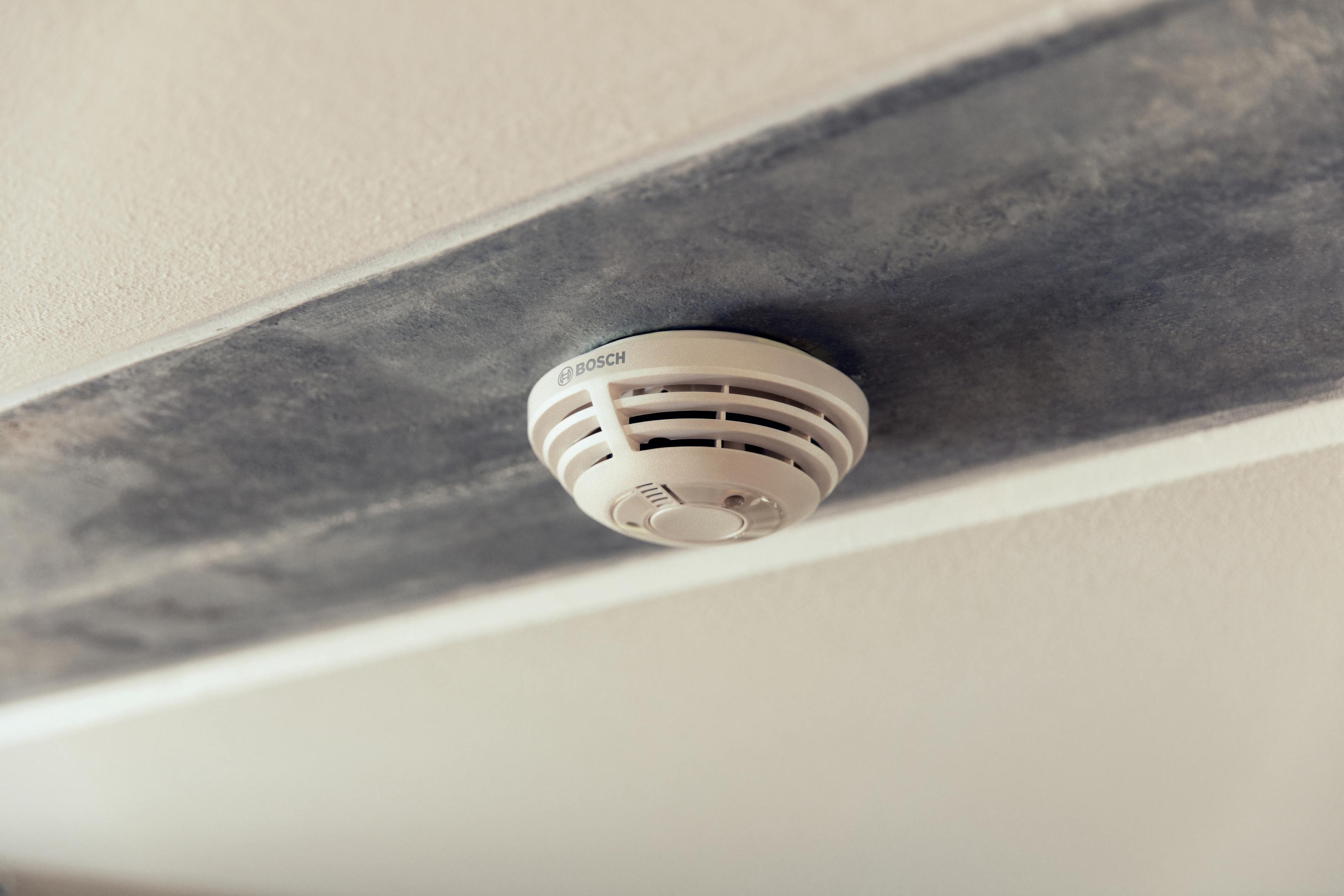 Ein Bosch-Rauchmelder an einer weißen Decke mit grauer Verkleidung befestigt.