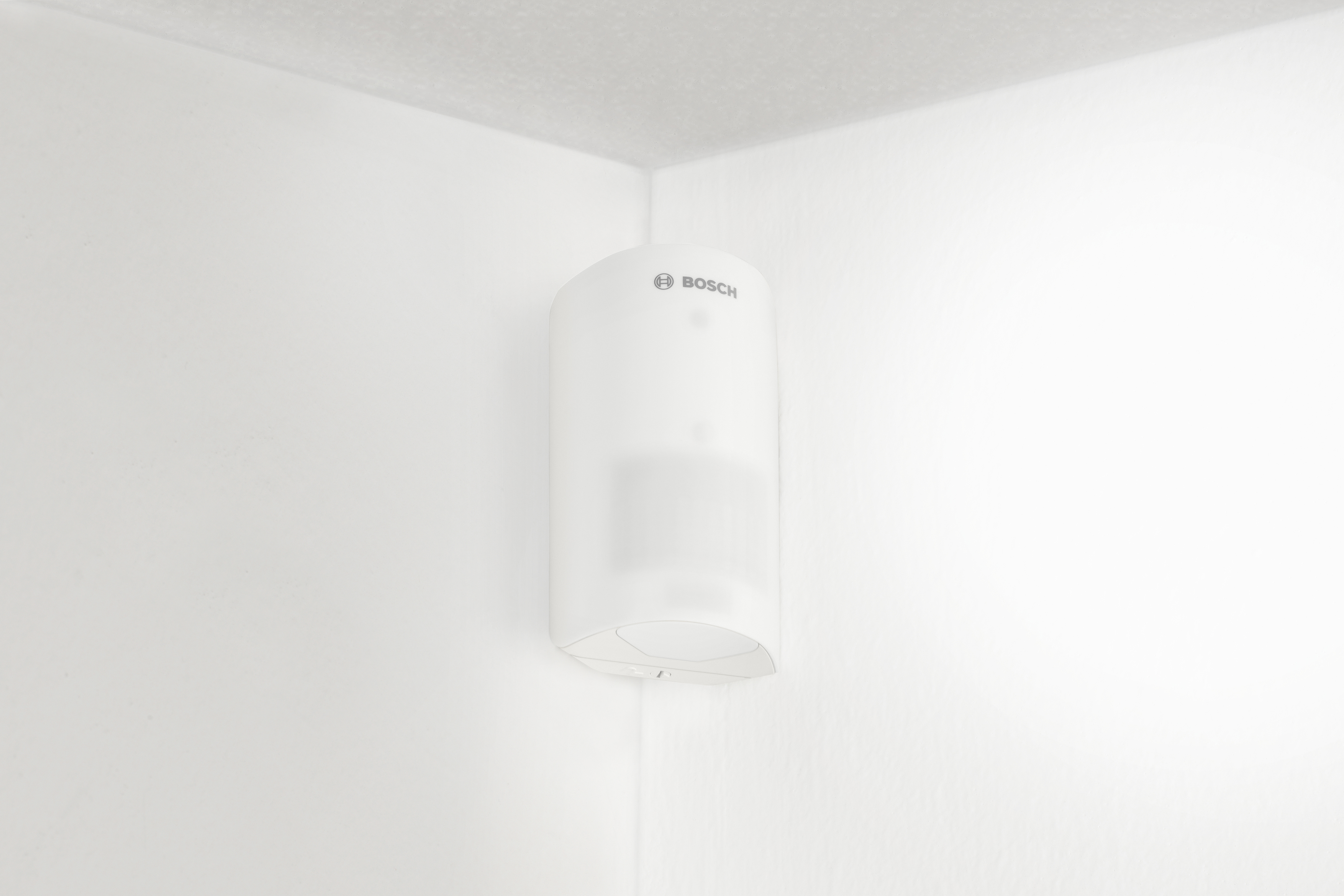 Ein weißer Bosch-Bewegungsmelder an einer weißen Wandecke montiert. Es ist zylindrisch geformt.