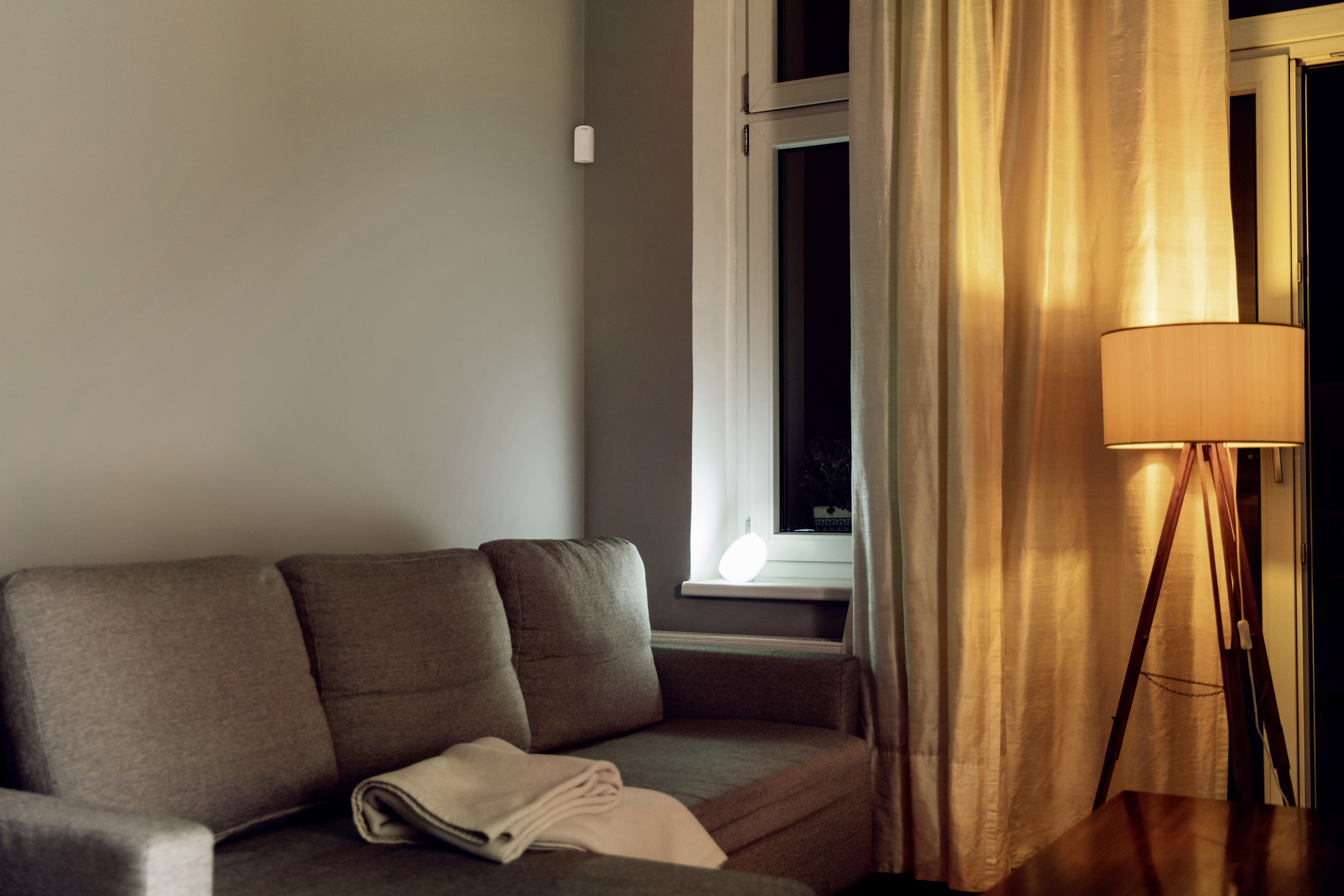 Innenaufnahme eines Wohnzimmers mit Sofa, Lampe, Fenster und einem weißen Licht.
