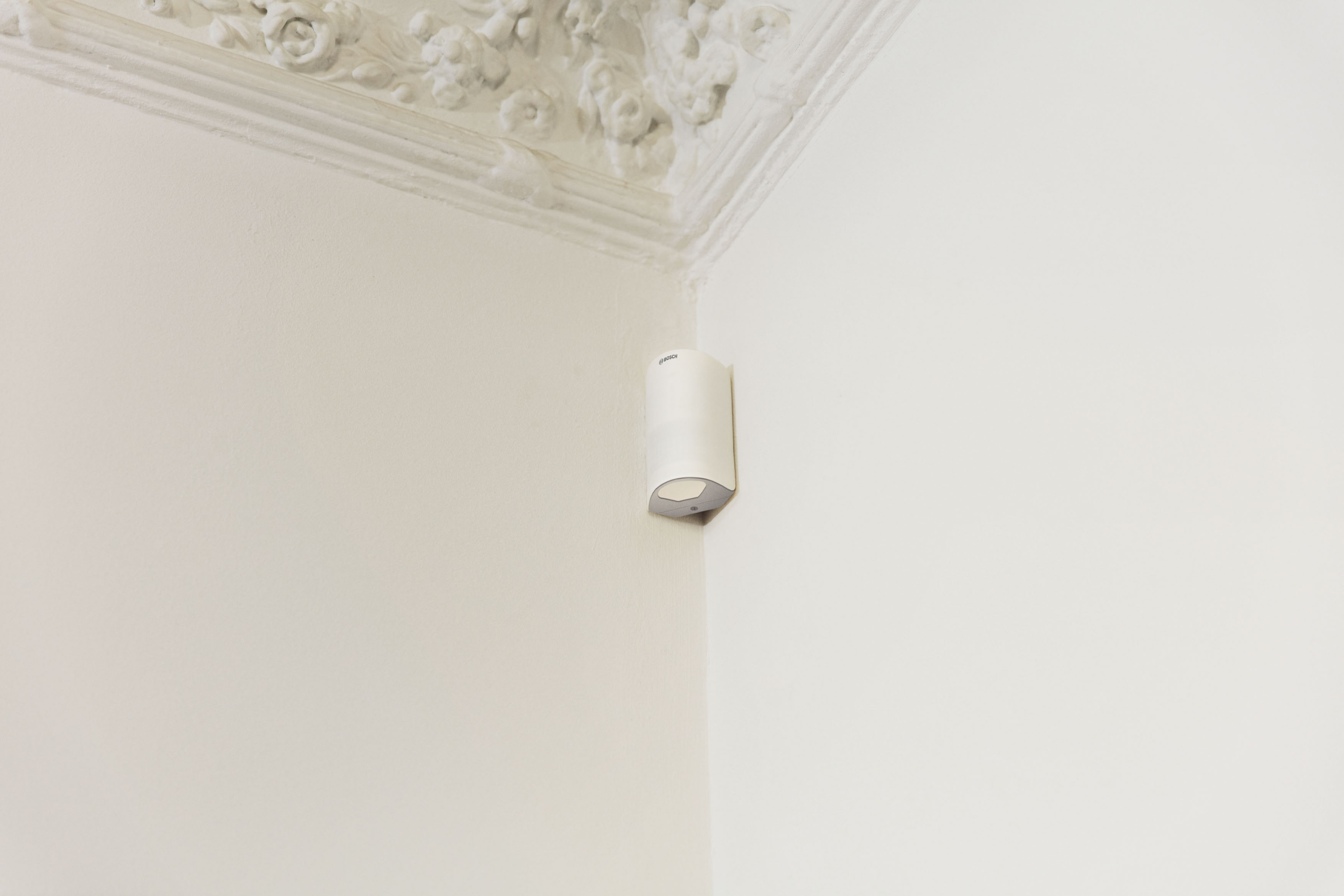 Weiße Wand mit Ecke. An der Ecke ist eine weiße Lampe montiert. Die Decke hat dekorative Leisten.