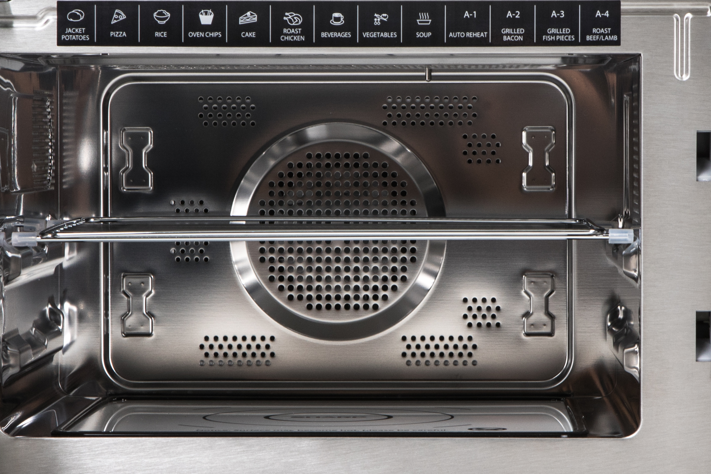 The inside of a stainless steel microwave oven. The top has icons, a shelf, and vents.
