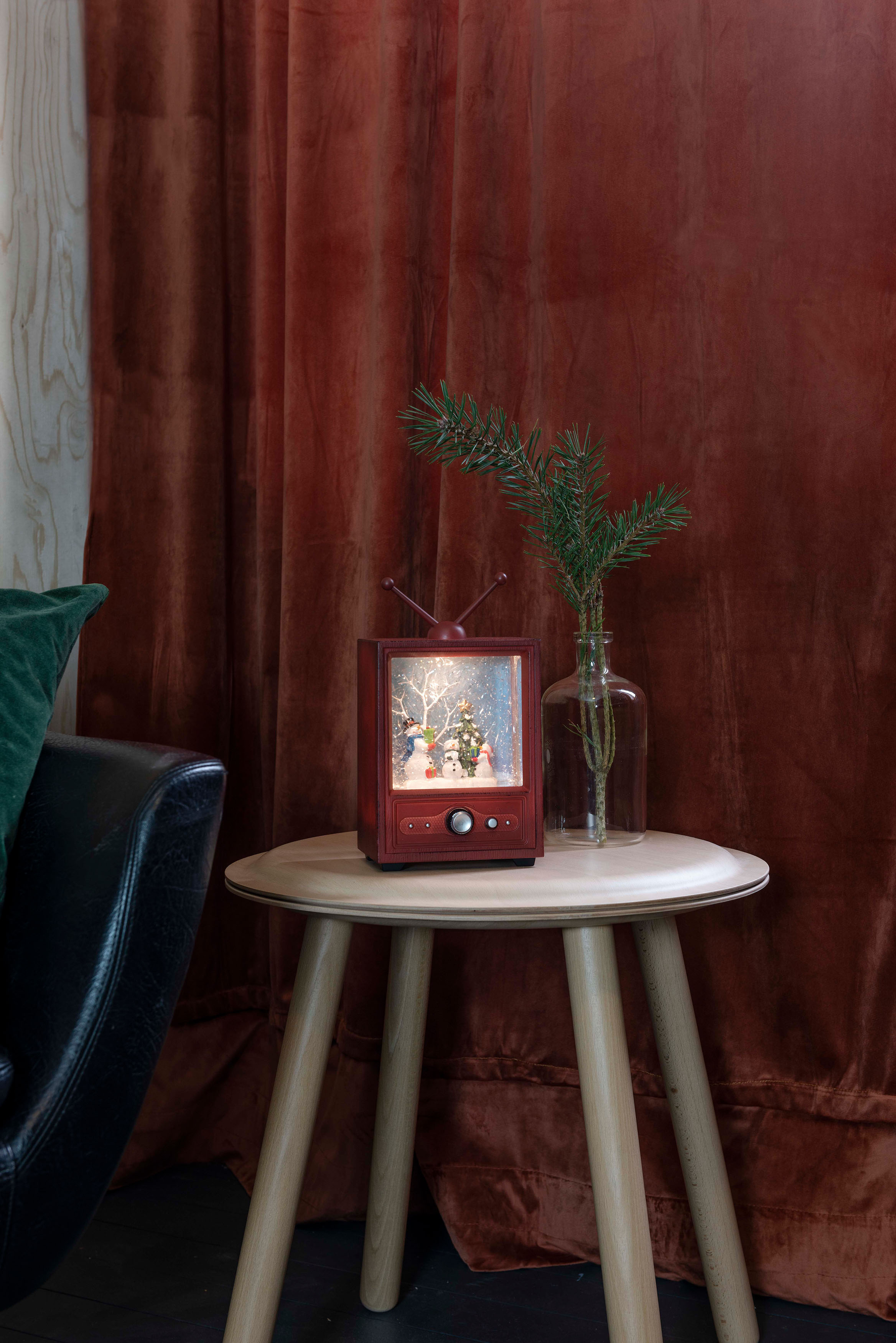 Eine dekorative Weihnachtsszene in einer Schneekugel auf einem Tisch. Hintergrund: roter Samtvorhang.