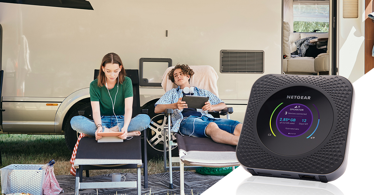 Zwei Personen nutzen Tablets in der Nähe eines mobilen Routers vor einem Wohnmobil. Der Router zeigt Daten an.