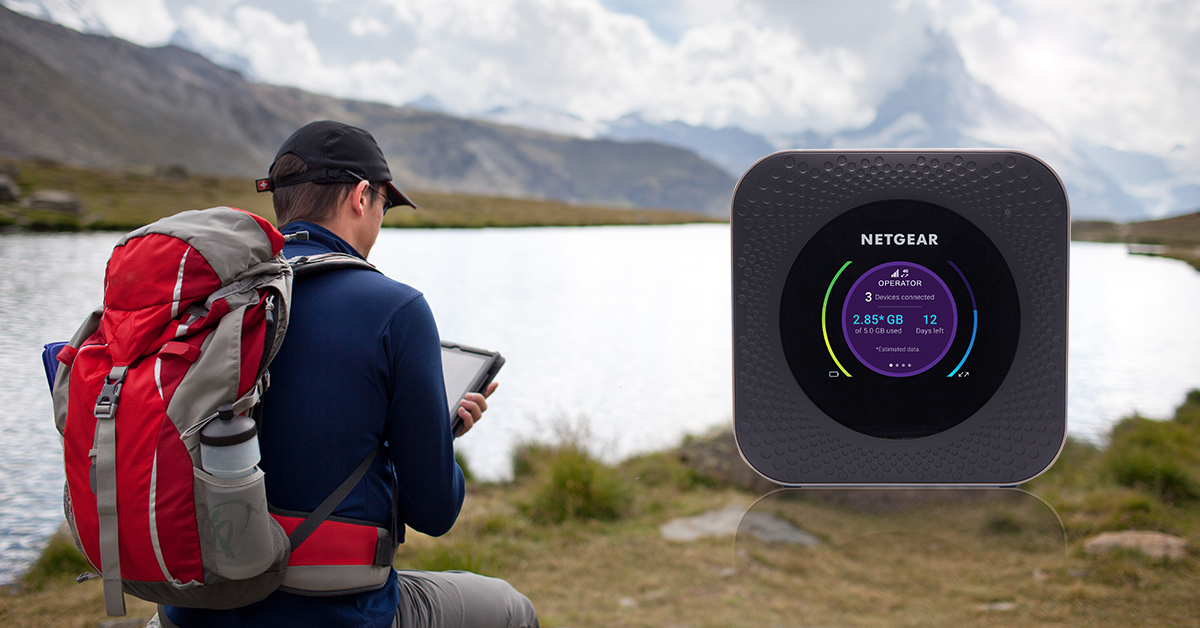 Mann benutzt ein mobiles Hotspot-Gerät in der Nähe eines Sees mit Rucksack und Tablet.