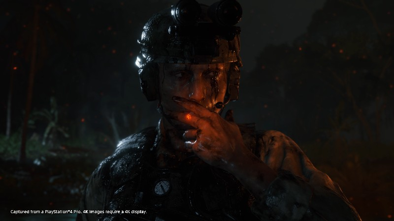 Soldado con casco, rostro cubierto de barro, mirando su mano con luz naranja.