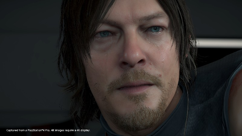 Primer plano de un hombre con cabello oscuro y barba, ligera sonrisa y ojos llorosos.