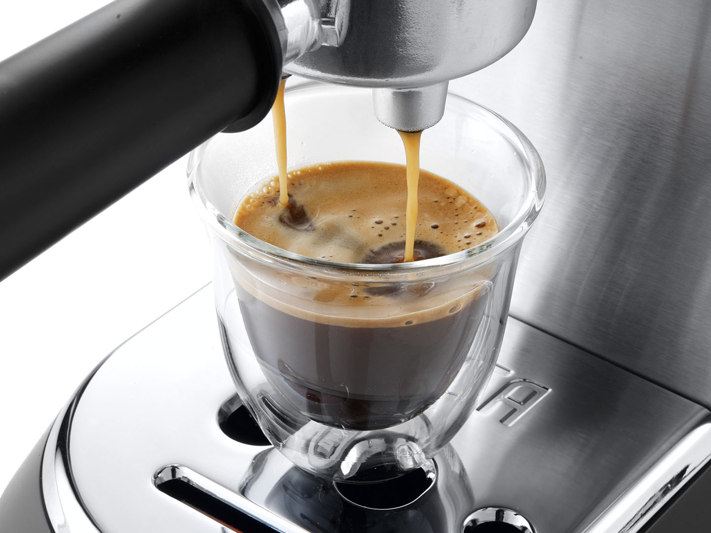Espresso makinesi, kahveyi şeffaf bir bardağa döküyor. Kahve koyu kahverengi.