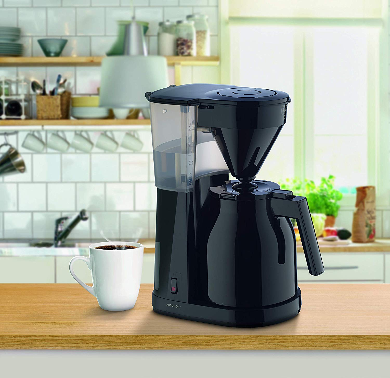Caffettiera nera con tazza bianca su tavolo di legno. Sfondo cucina visibile.