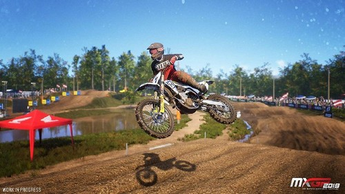 Piloto de motocross en el aire. Piloto y moto en el aire sobre una pista de tierra. Tienda roja al fondo.