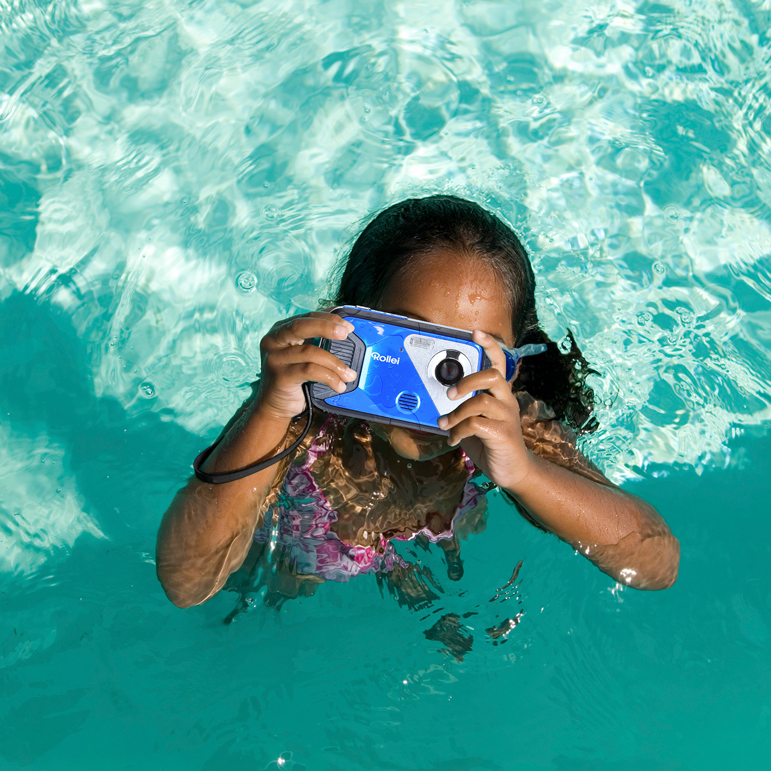 Een meisje maakt een foto onder water met een blauw-witte camera in een zwembad.