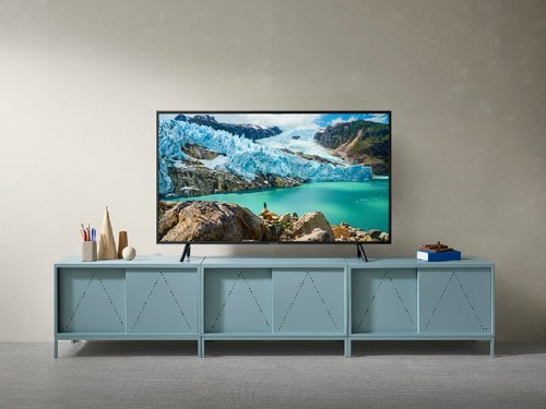 Televisor grande sobre un mueble azul. Se muestra una escena paisajística. El fondo es una pared beige claro.