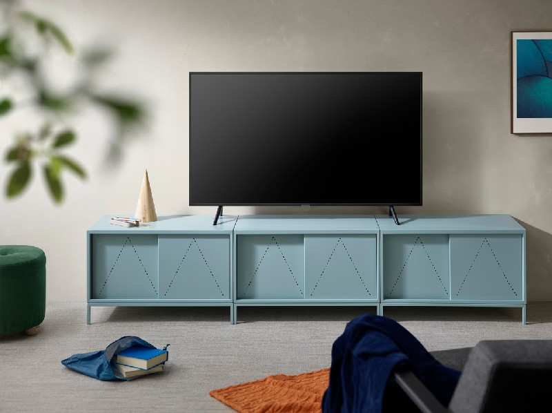 Salón: TV en mueble azul, taburete verde, alfombra naranja, sofá gris, primer plano borroso.