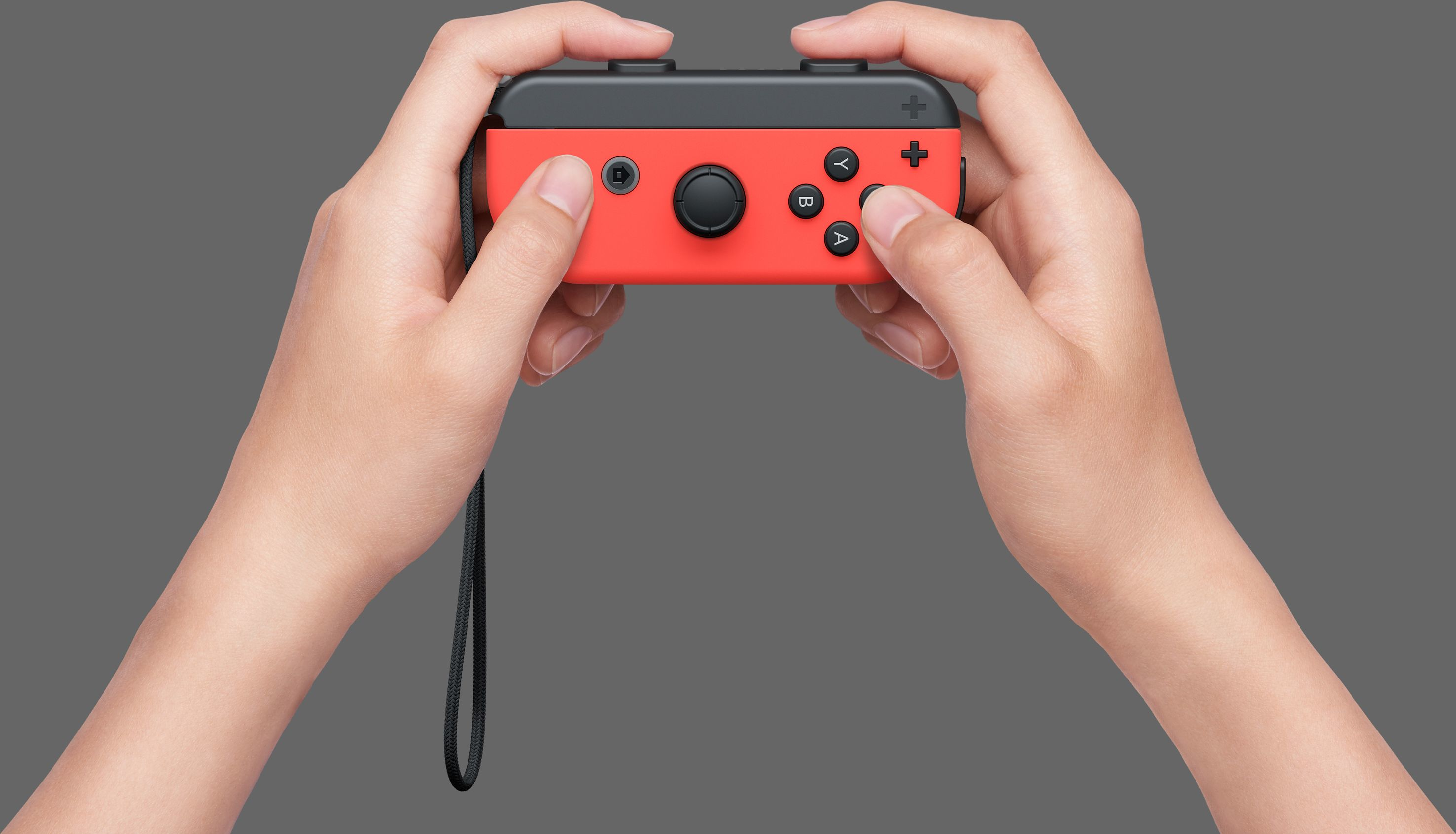 Hände halten einen roten Nintendo Switch Joy-Con-Controller auf grauem Hintergrund.