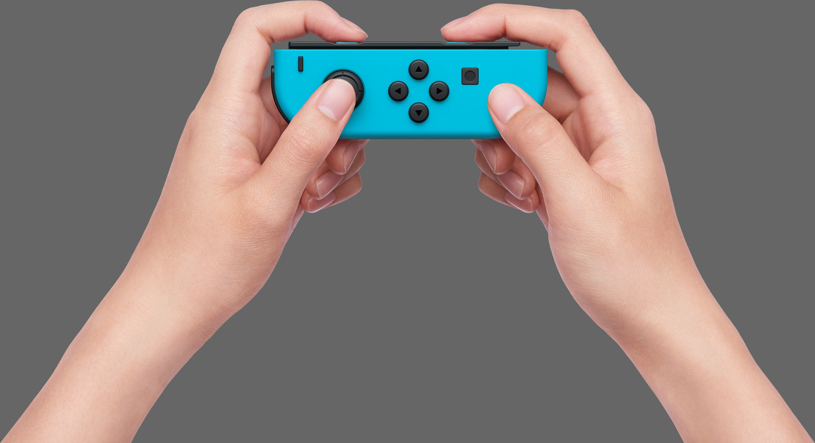 Hände halten einen hellblauen Gamecontroller mit schwarzen Knöpfen. Ein Daumen liegt auf dem linken Stick. Grauer Hintergrund.