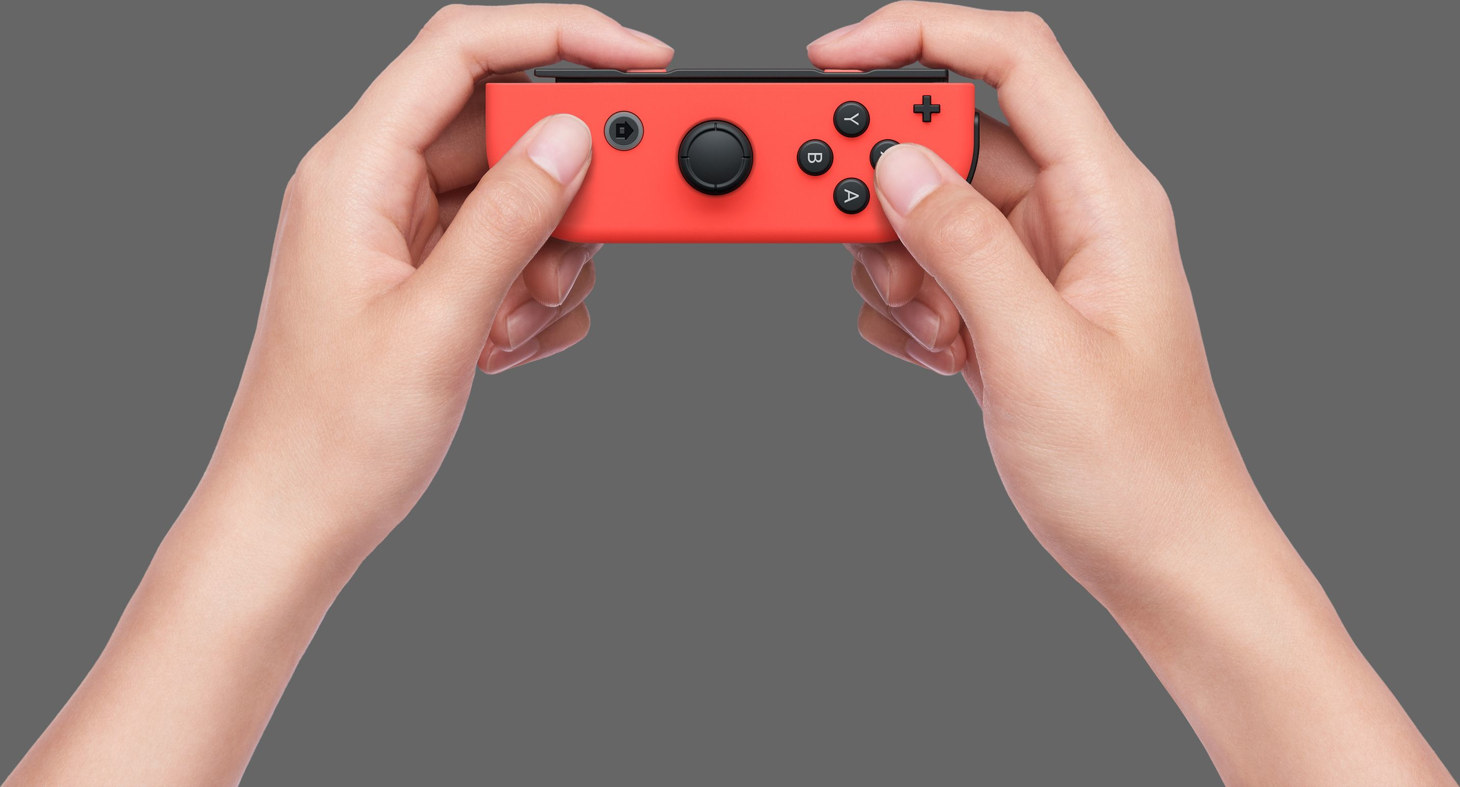 Zwei Hände halten einen roten Videospiel-Controller mit Knöpfen, auf grauem Hintergrund, Nahaufnahme.
