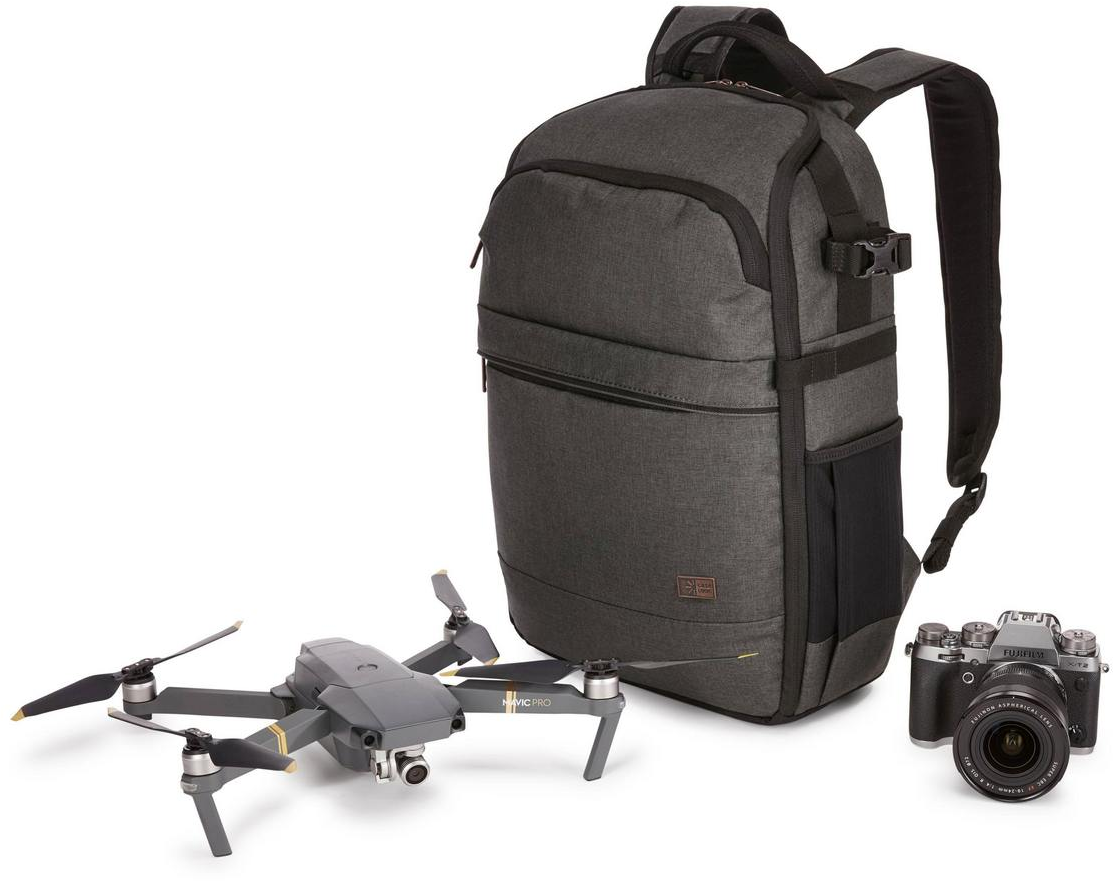 Drohne, Kamera und Rucksack auf weißer Oberfläche. Graue Drohne und schwarze Kamera sind sichtbar.