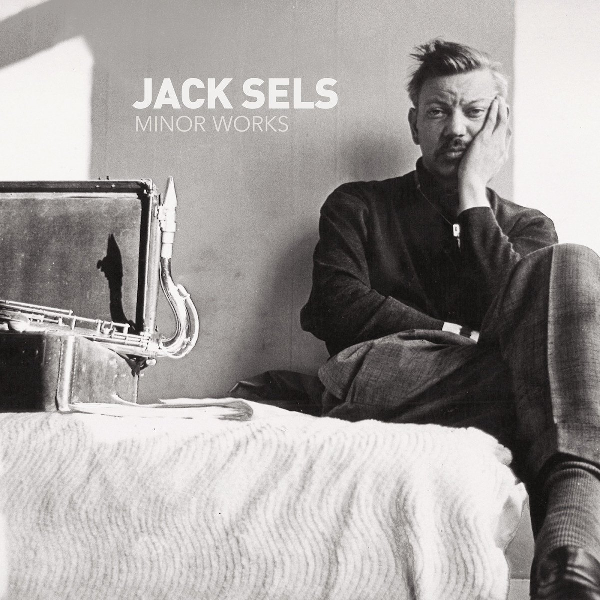 Couverture d'album en noir et blanc. Un homme avec la main sur le visage est assis à côté d'un saxophone.