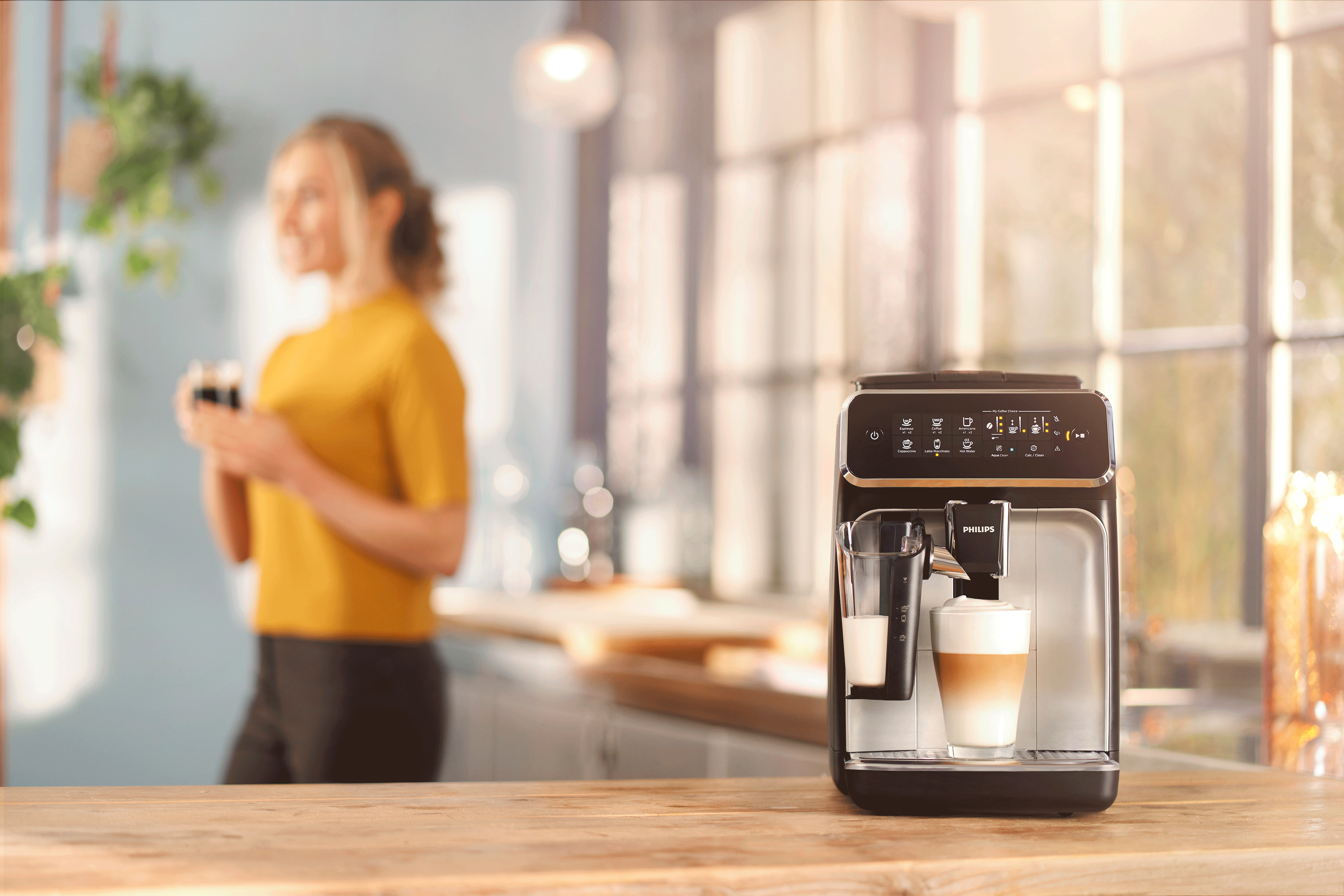 Eine Kaffeemaschine mit einer Frau im Hintergrund, auf einer hölzernen Arbeitsplatte.