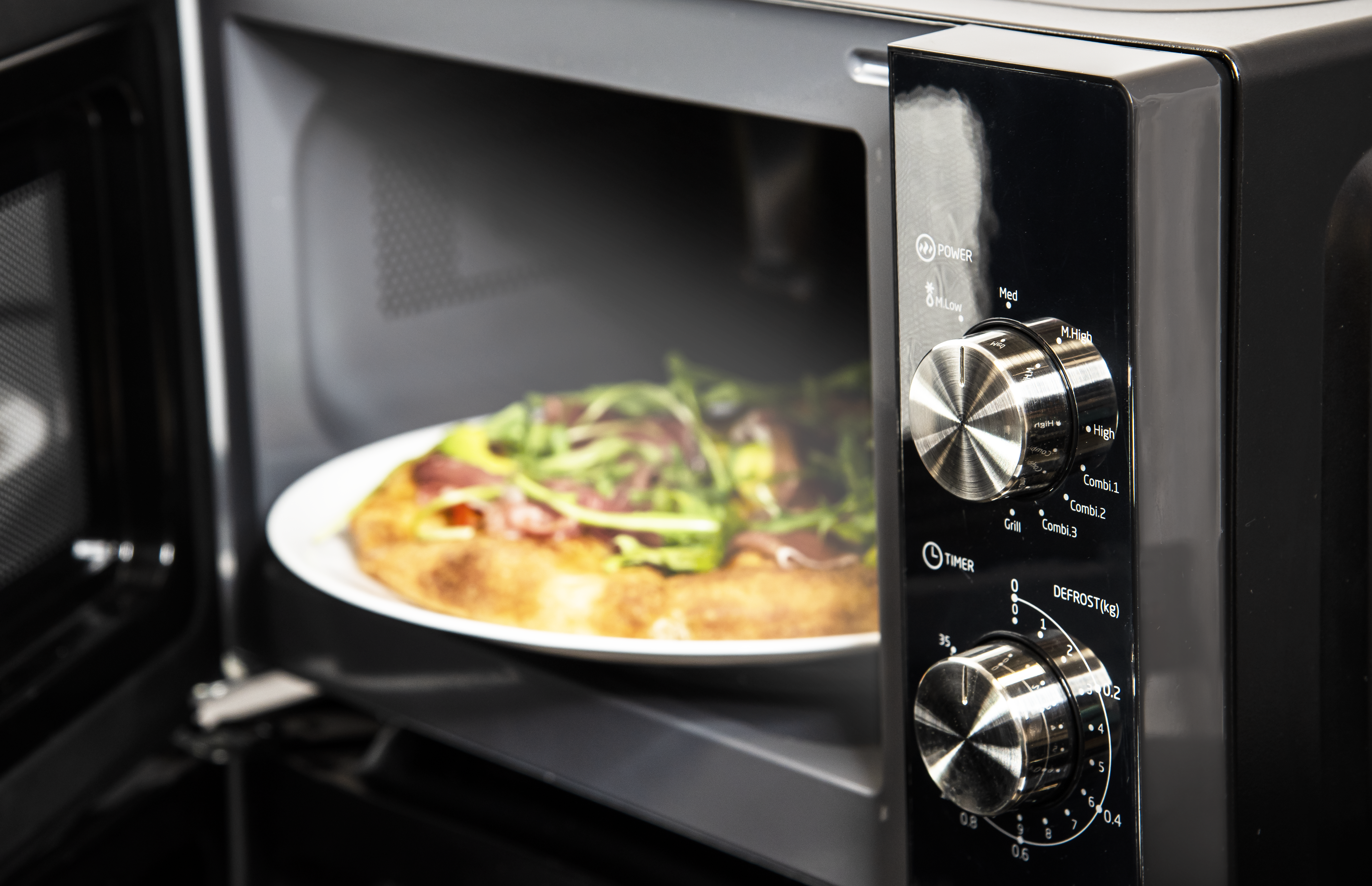 Four à micro-ondes avec pizza à l'intérieur. La porte est ouverte, montrant la pizza sur une assiette blanche.