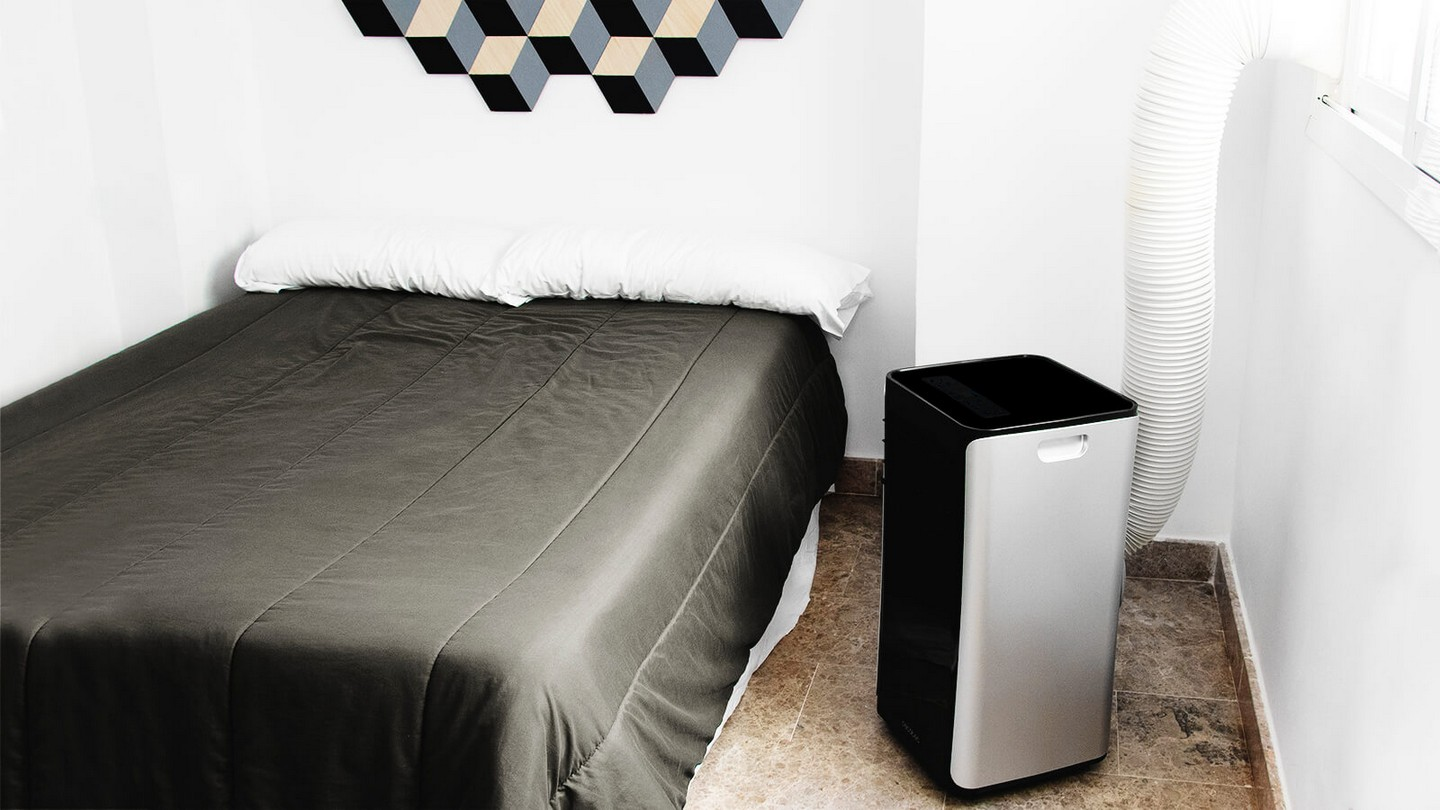 Dormitorio con aire acondicionado. Cama con manta gris. Paredes blancas y decoración de madera.