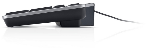 Seitenansicht einer schwarzen Tastatur mit silberner Umrandung. Ein Kabel ragt aus der Rückseite. Die Tastatur spiegelt sich.