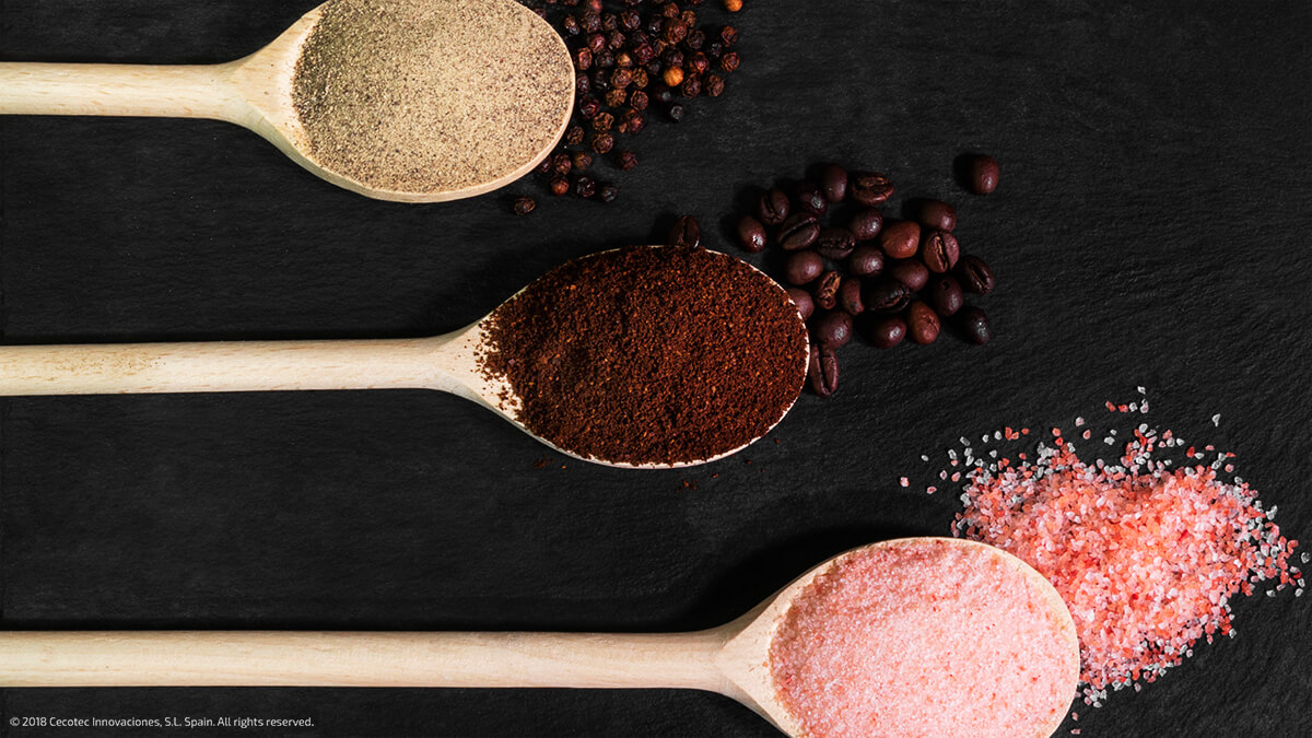 Cucharas de madera con pimienta, café molido y sal rosa sobre pizarra.