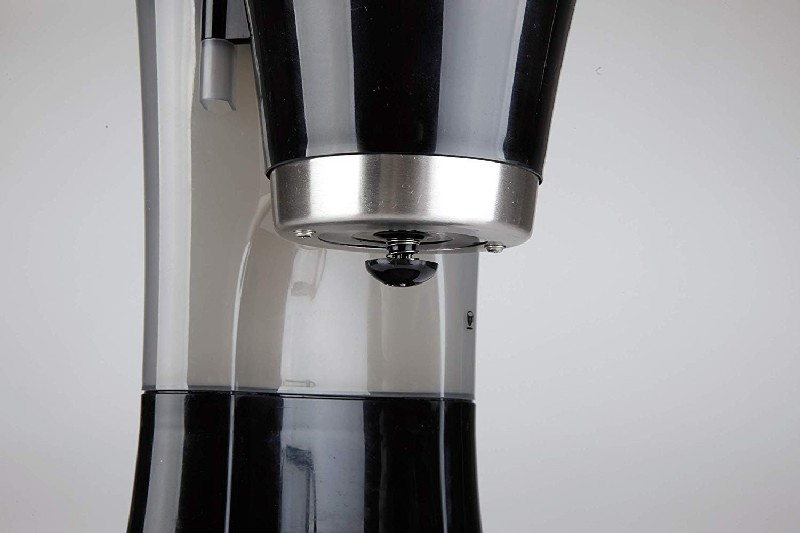 Primer plano de una máquina de espresso. Diseño negro y plateado con un botón negro y una boquilla. Fondo blanco.