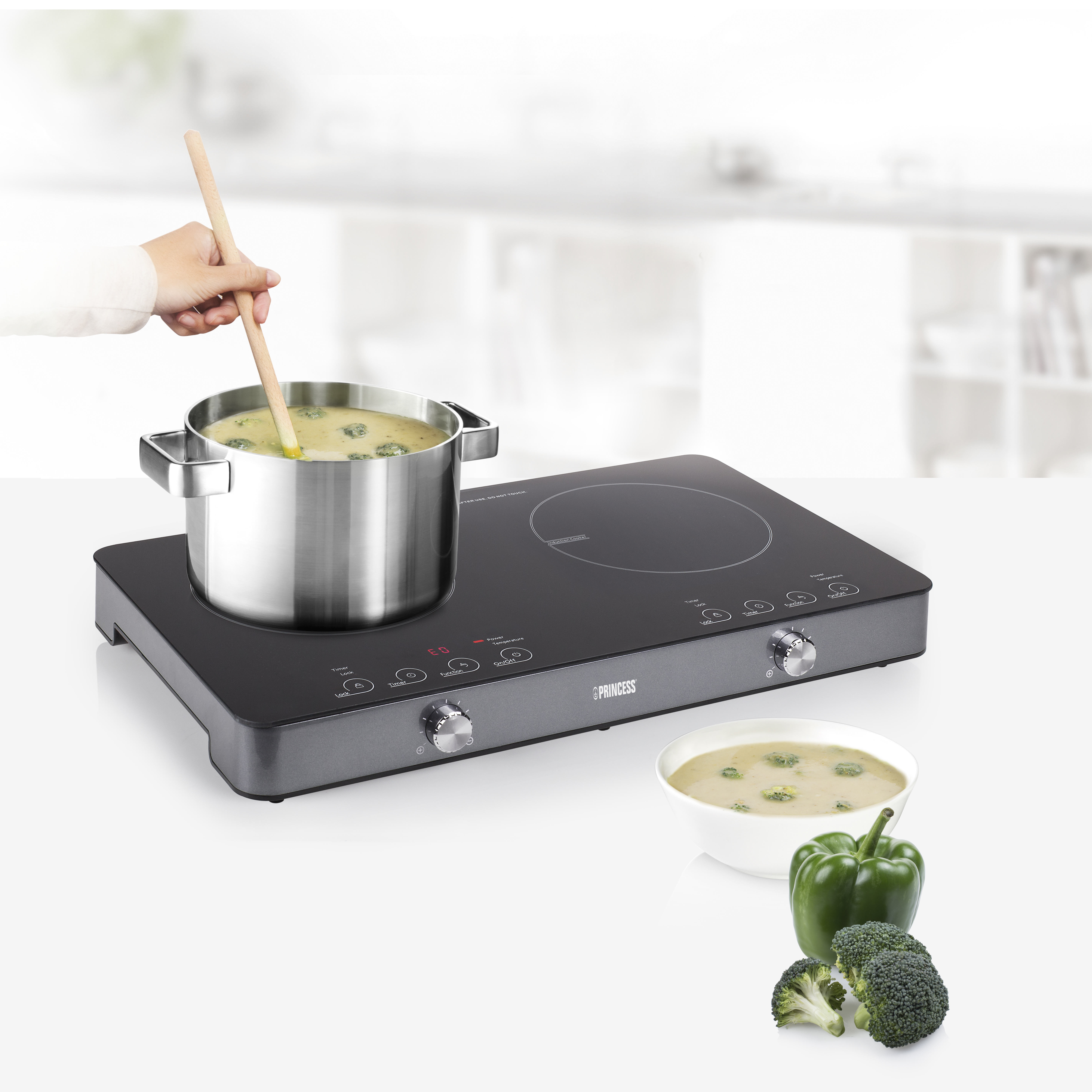 Een persoon roert soep in een pan op een zwarte inductiekookplaat. Broccoli, paprika en kom.