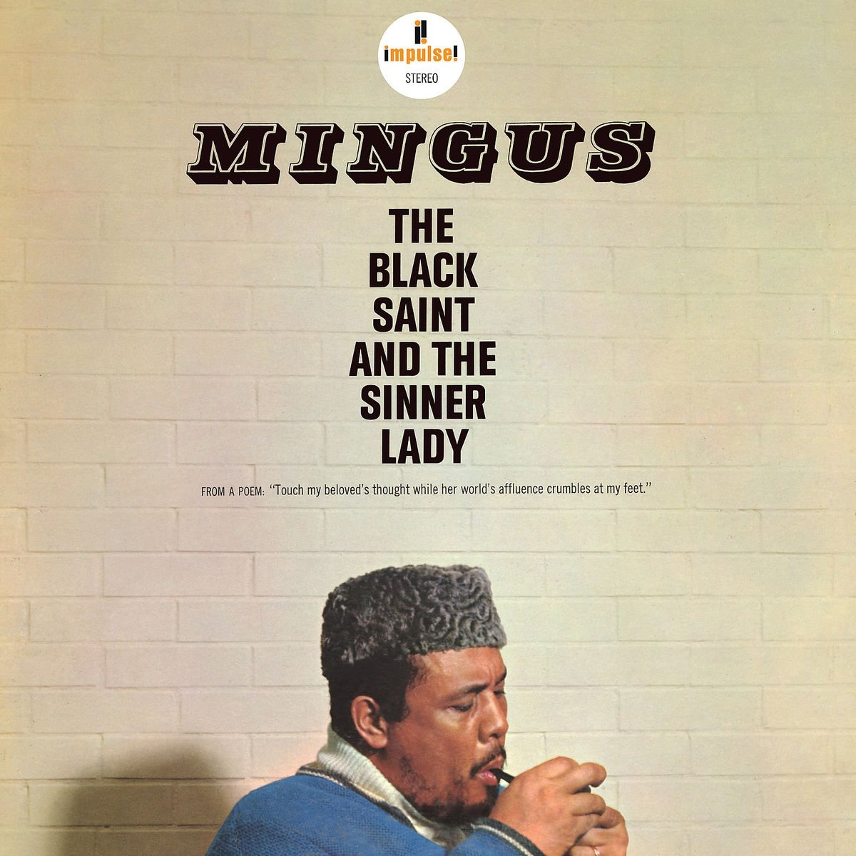 Albumhoes van Mingus. Een man steekt een sigaret aan. Tekst in het midden op een bakstenen muur.