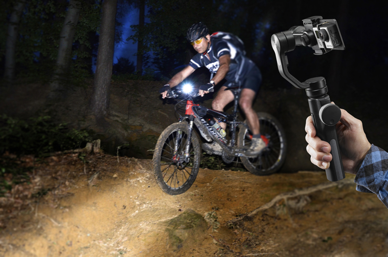 Ein Radfahrer fährt nachts mit einem Mountainbike durch einen Wald. Eine Hand hält einen Kamerastabilisator.