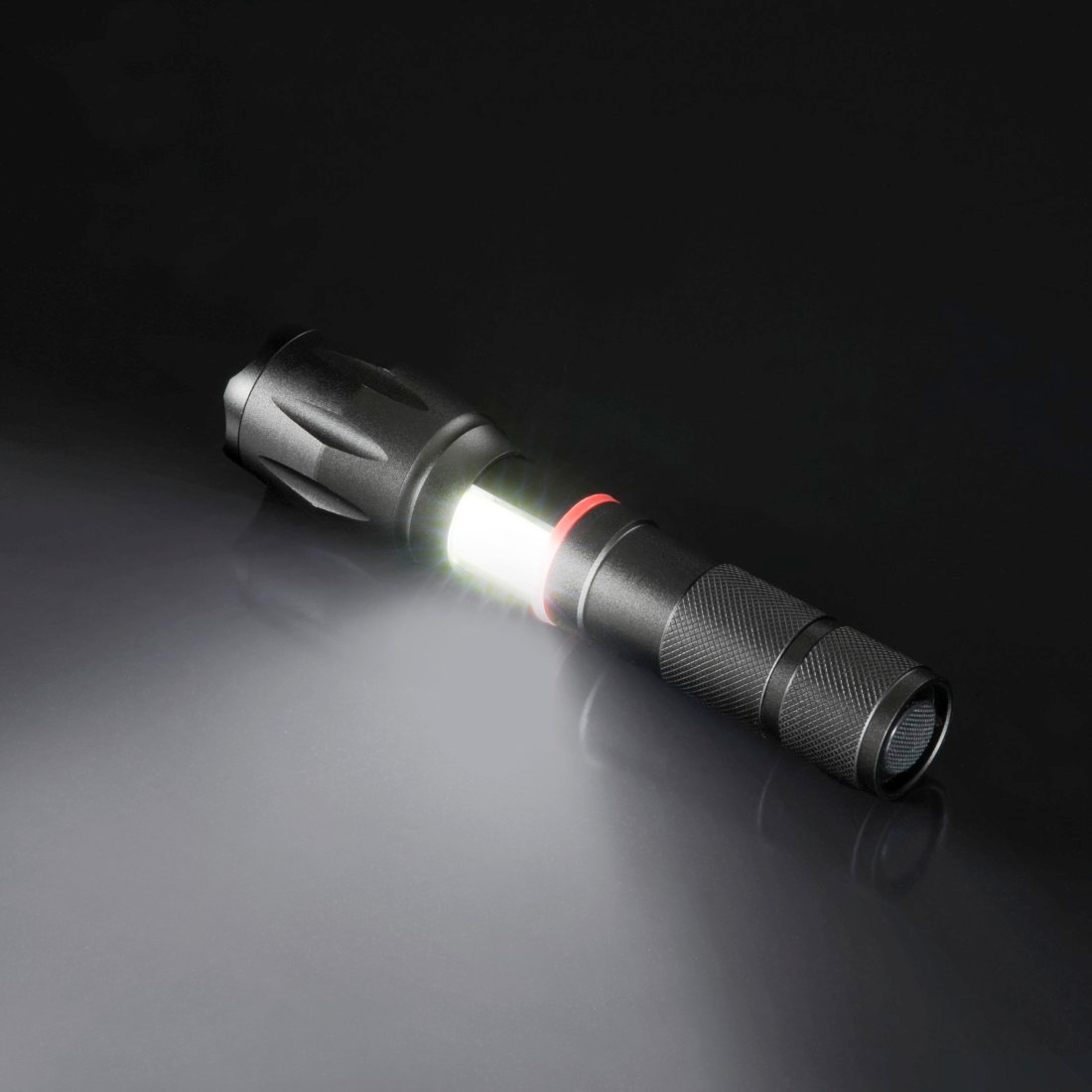 Une lampe de poche noire avec un faisceau de lumière blanche brillante. Elle est sur une surface sombre, reflétant la lumière.