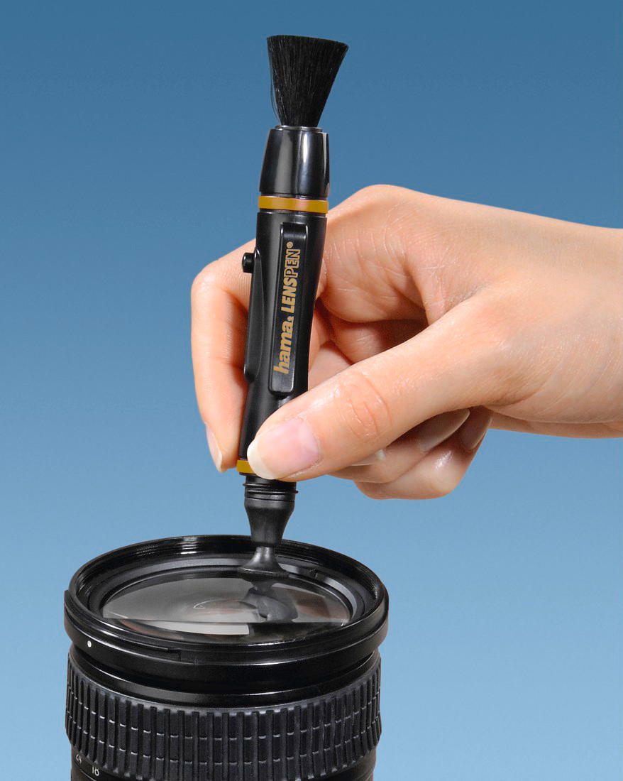 Une main nettoie une lentille d'appareil photo avec un stylo d'objectif. L'objectif est noir, le fond est bleu.