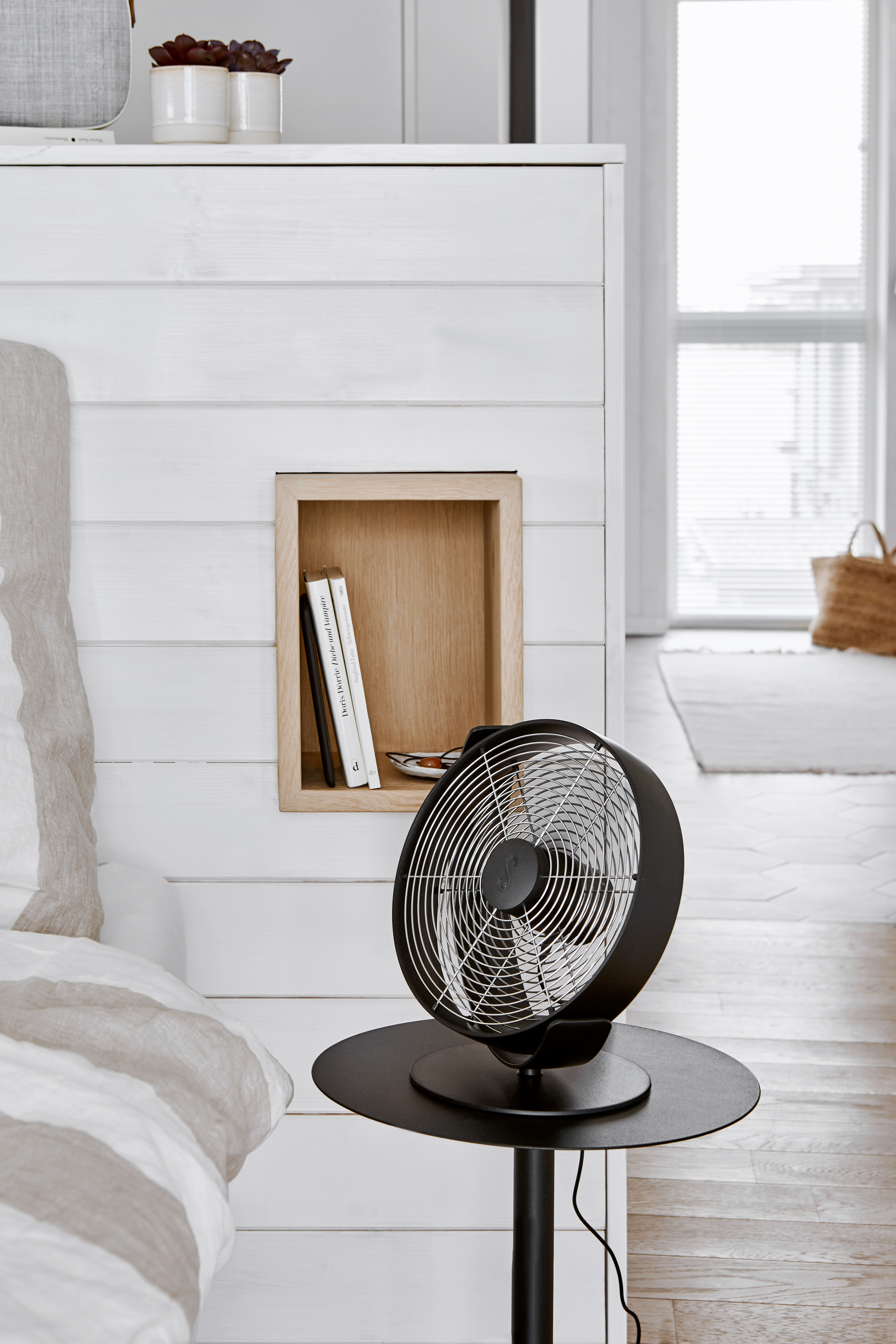 Schwarzer Ventilator auf Ständer, Holz-Nische in weißer Wand.