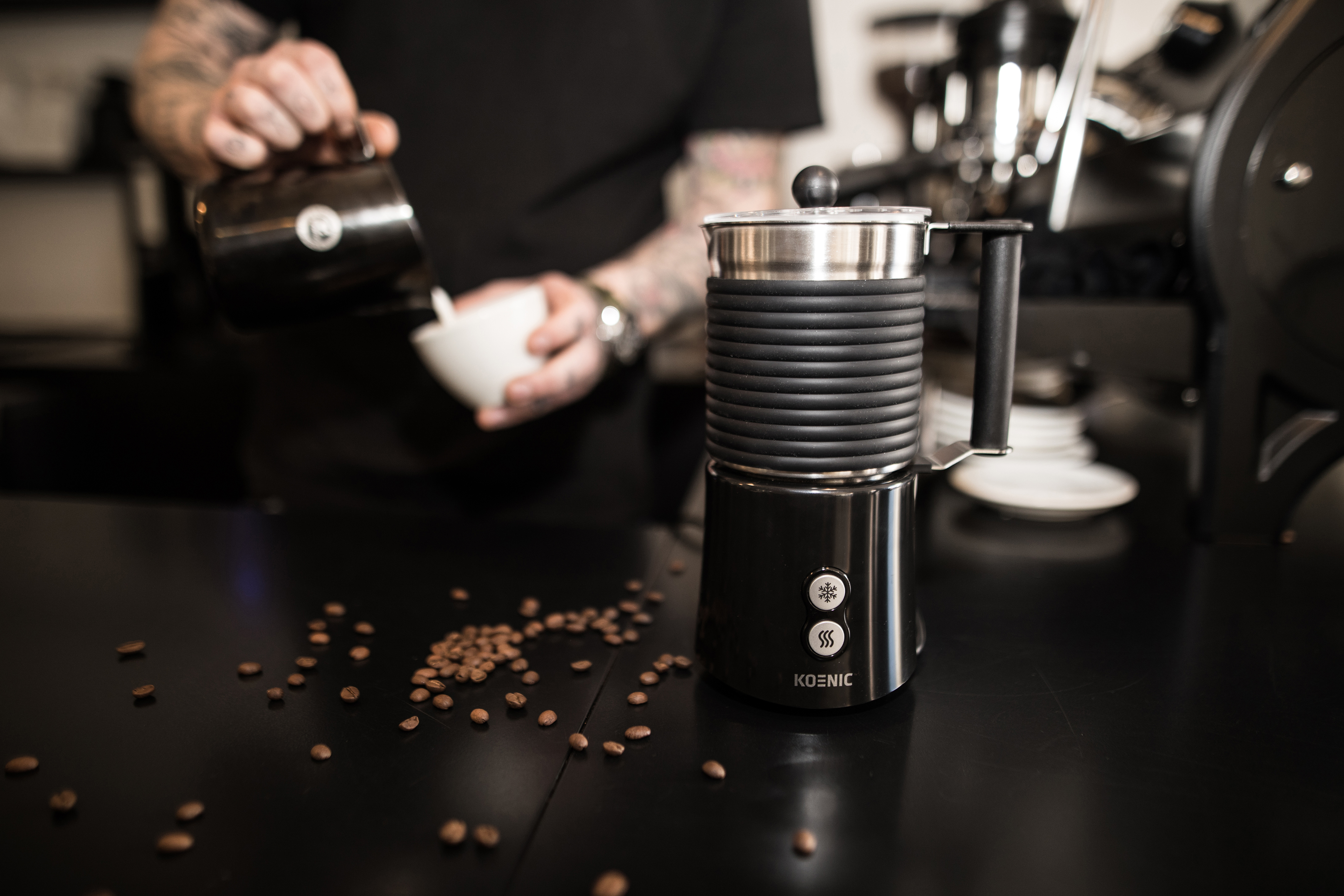 Barista gießt Milch in eine Tasse in der Nähe eines schwarzen Milchaufschäumers.