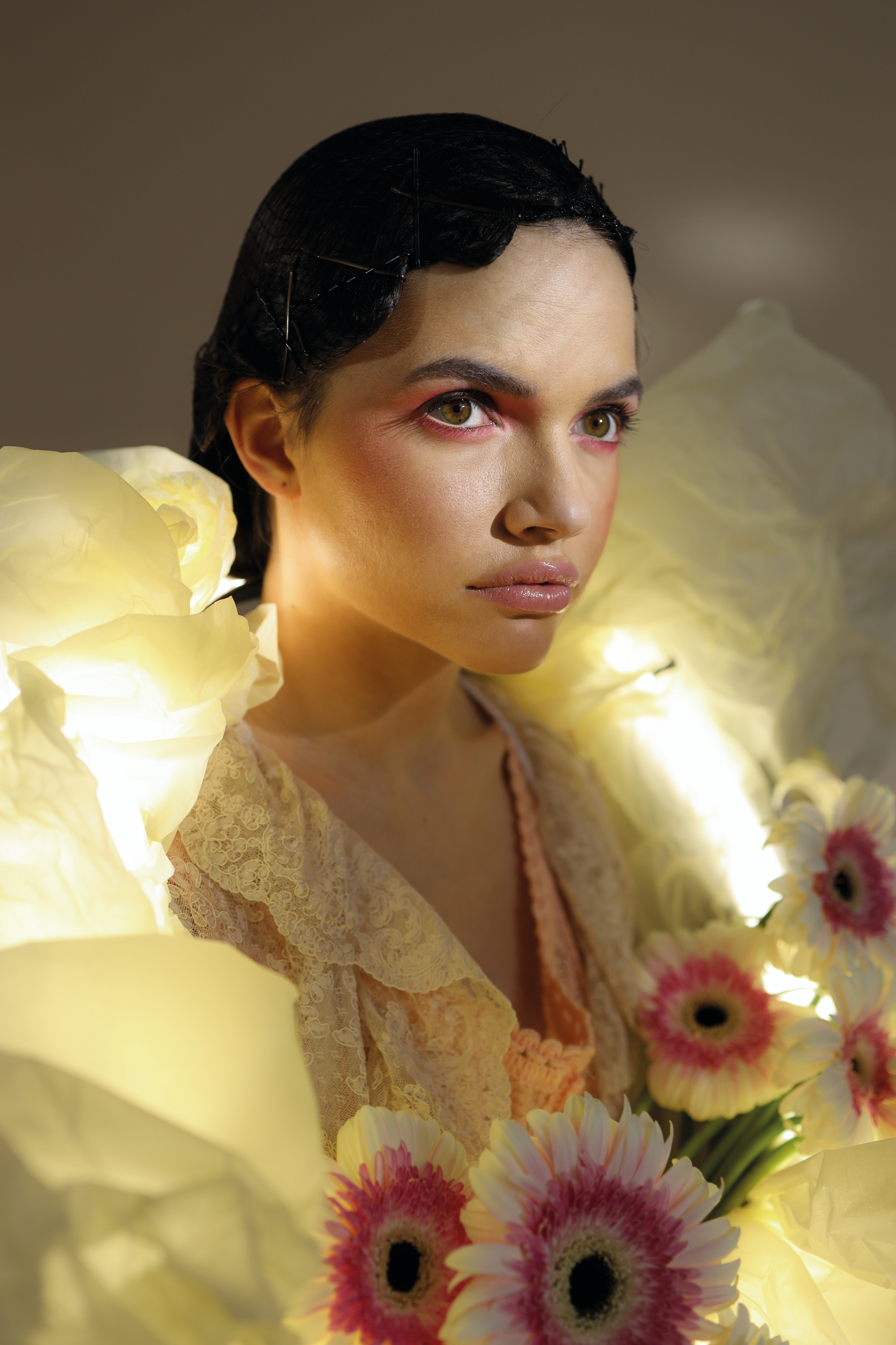 Frau mit leichtem Make-up, umgeben von Blumen, die zur Seite blickt.