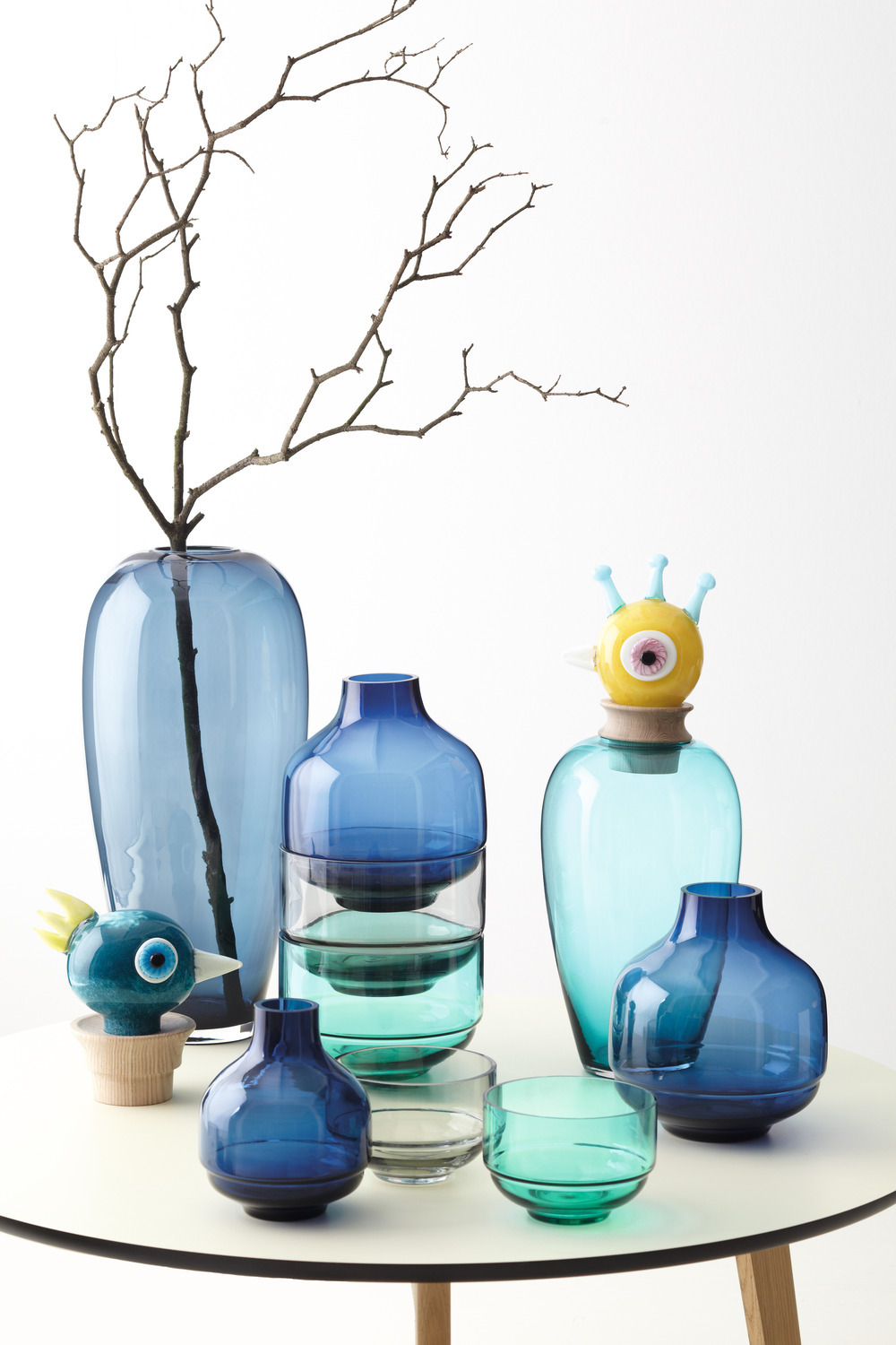 Verschiedene blaue Glasvasen und dekorative Objekte auf einem weißen Tisch angeordnet.