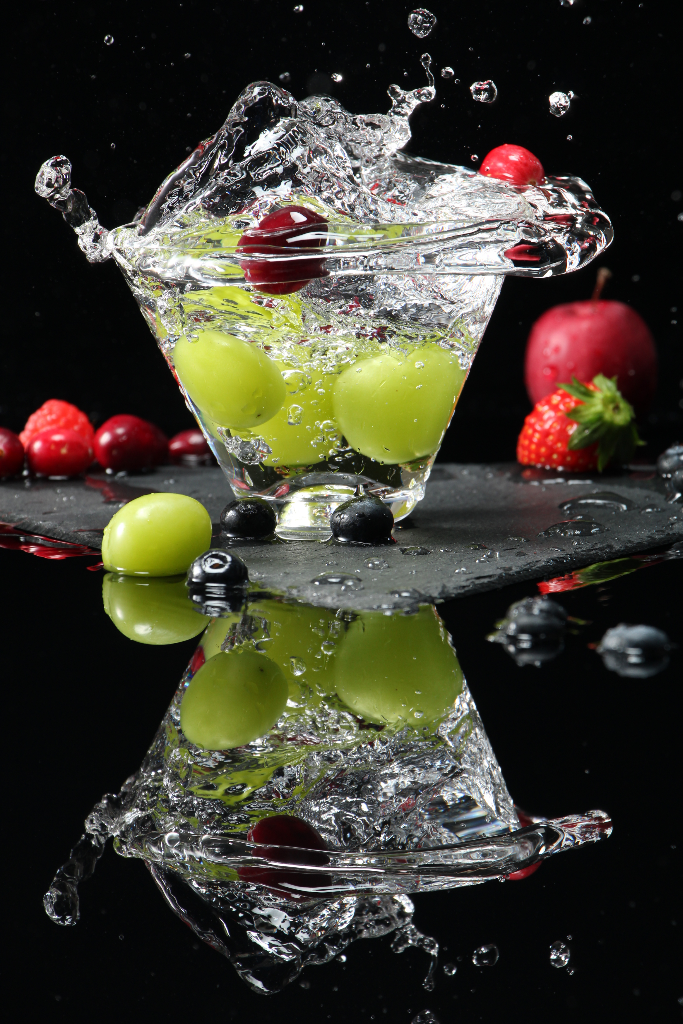 Ein Wasserspritzer mit grünen Trauben und Beeren. Die Reflexion ist ebenfalls sichtbar.