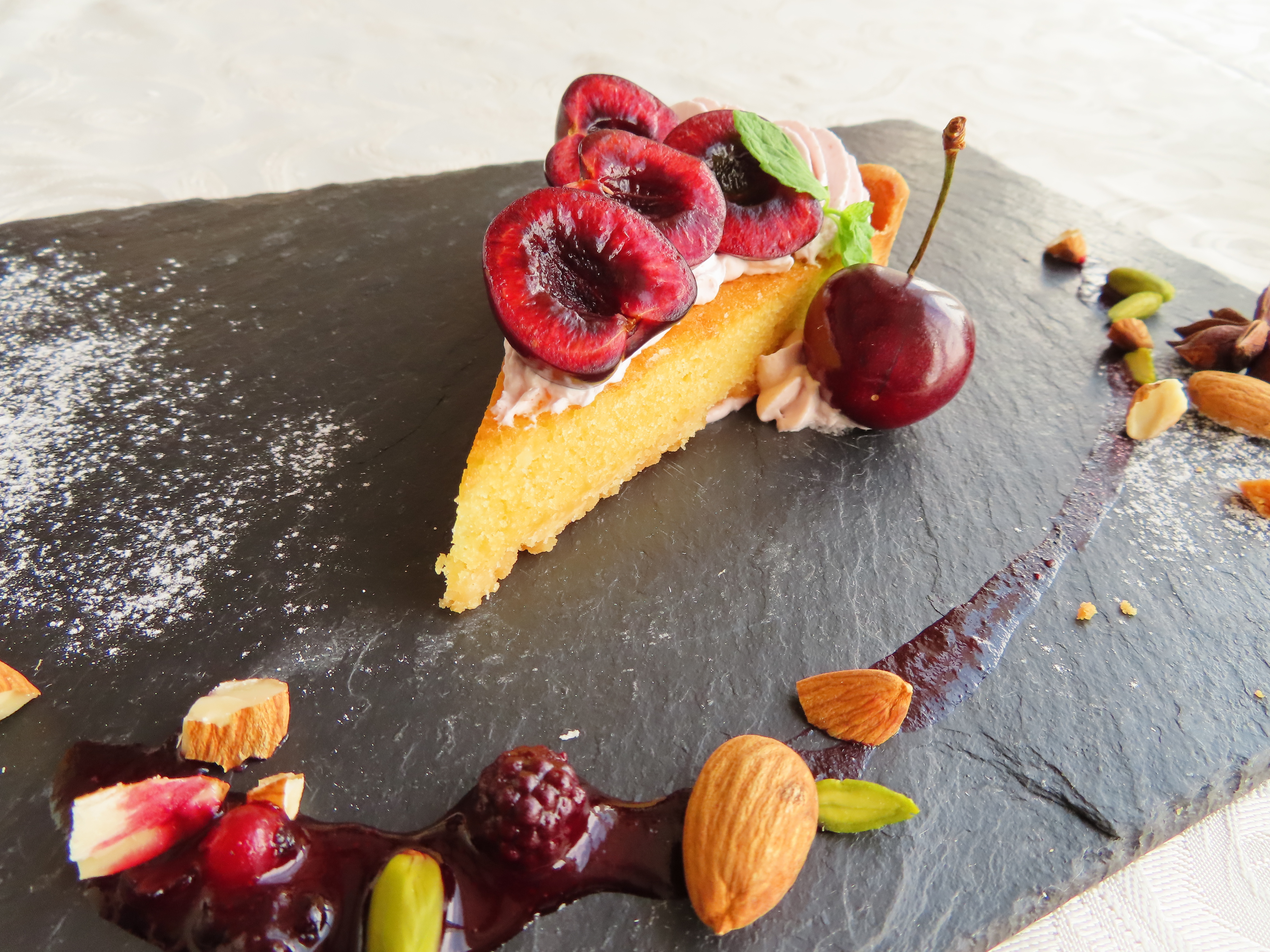 Ein Kuchenstück mit Kirschen, Beeren und Nüssen auf einem schwarzen Schieferteller.