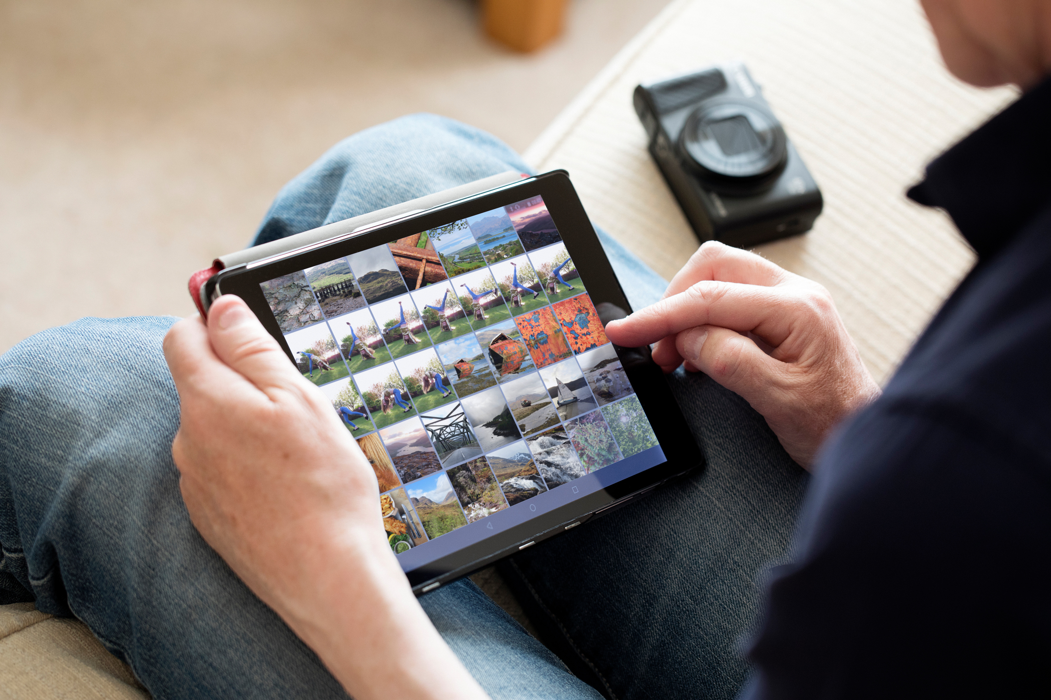 Eine Person, die ein Tablet auf dem Schoß benutzt und Fotos ansieht. Eine Kamera daneben.