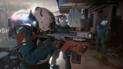 Tres médicos con cascos y uniformes verde azulado con armas, uno apuntando. El fondo es un edificio.